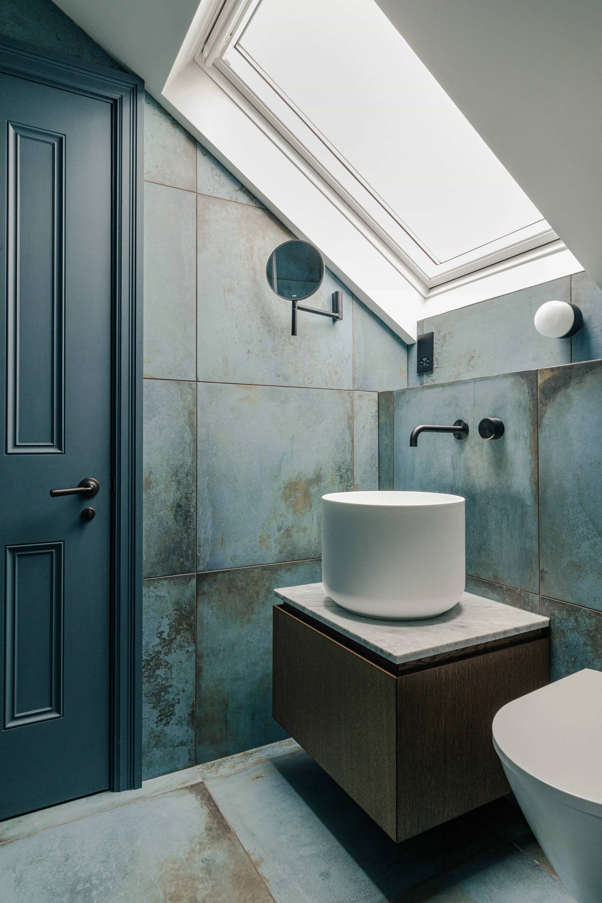 Atmospheric micro-cement powder room with a white cylindrical basin vanity set under a skylight window, Love Locations SW13.