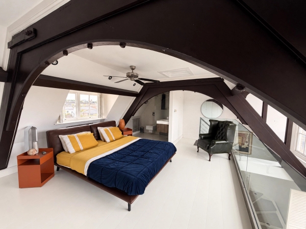 Atmospheric master bedroom set beneath dramatic exposed dark timber roof trusses in a Brixton SW4 penthouse location, available through Love Locations.