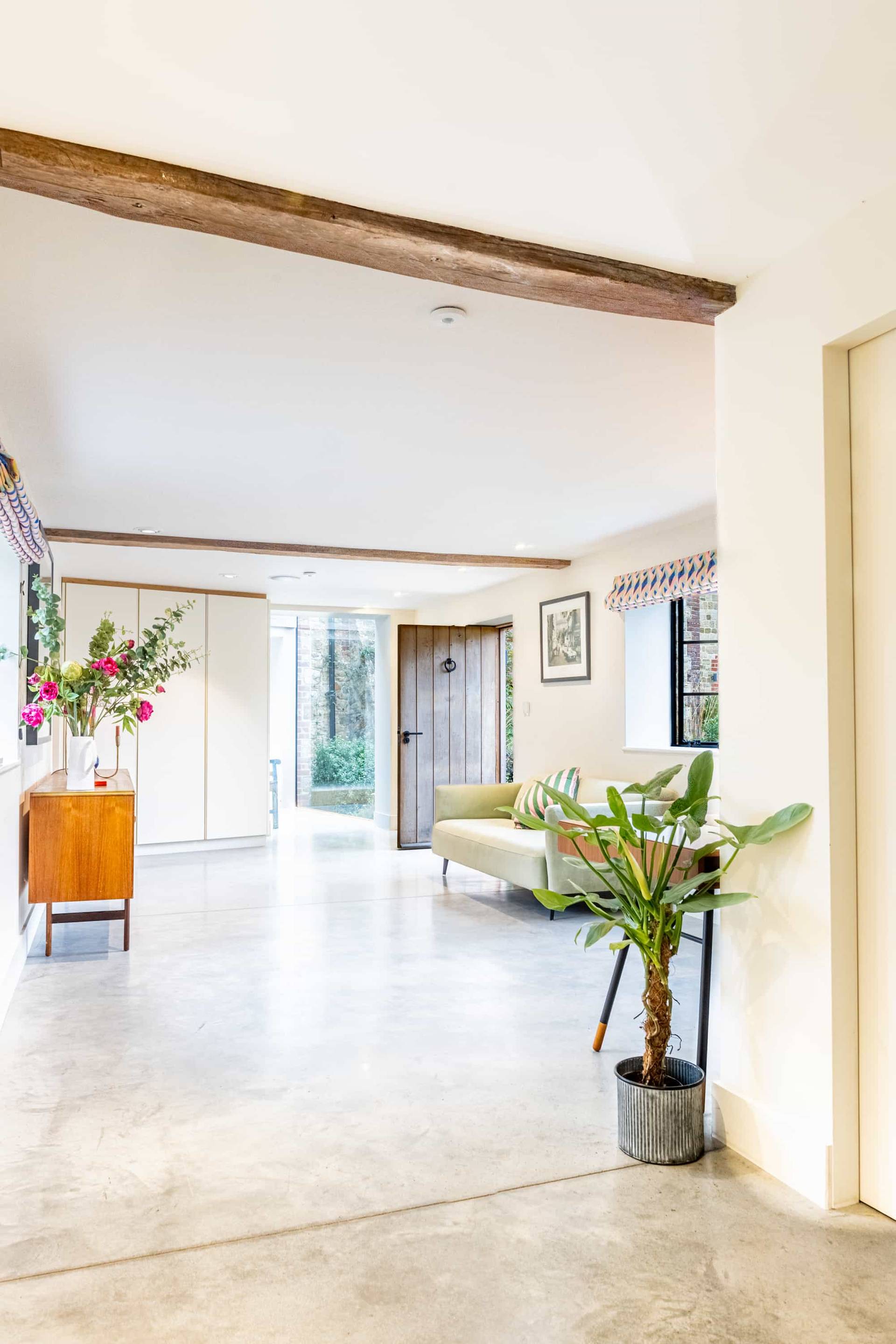 Bright living room corner with light wood floors, green potted plant, and warm timber door accents, Love Locations GU28.