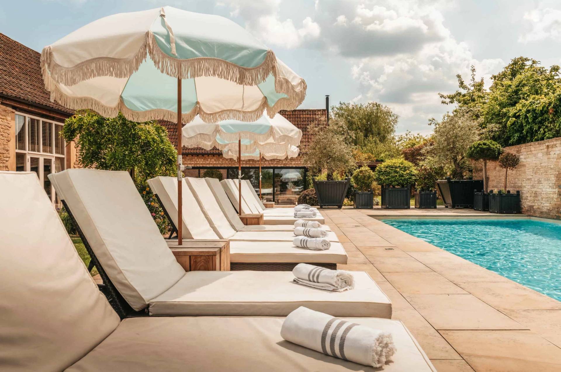 Mediterranean resort-style poolside loungers with striped rolled towels and pastel fringed umbrellas through Love Locations.