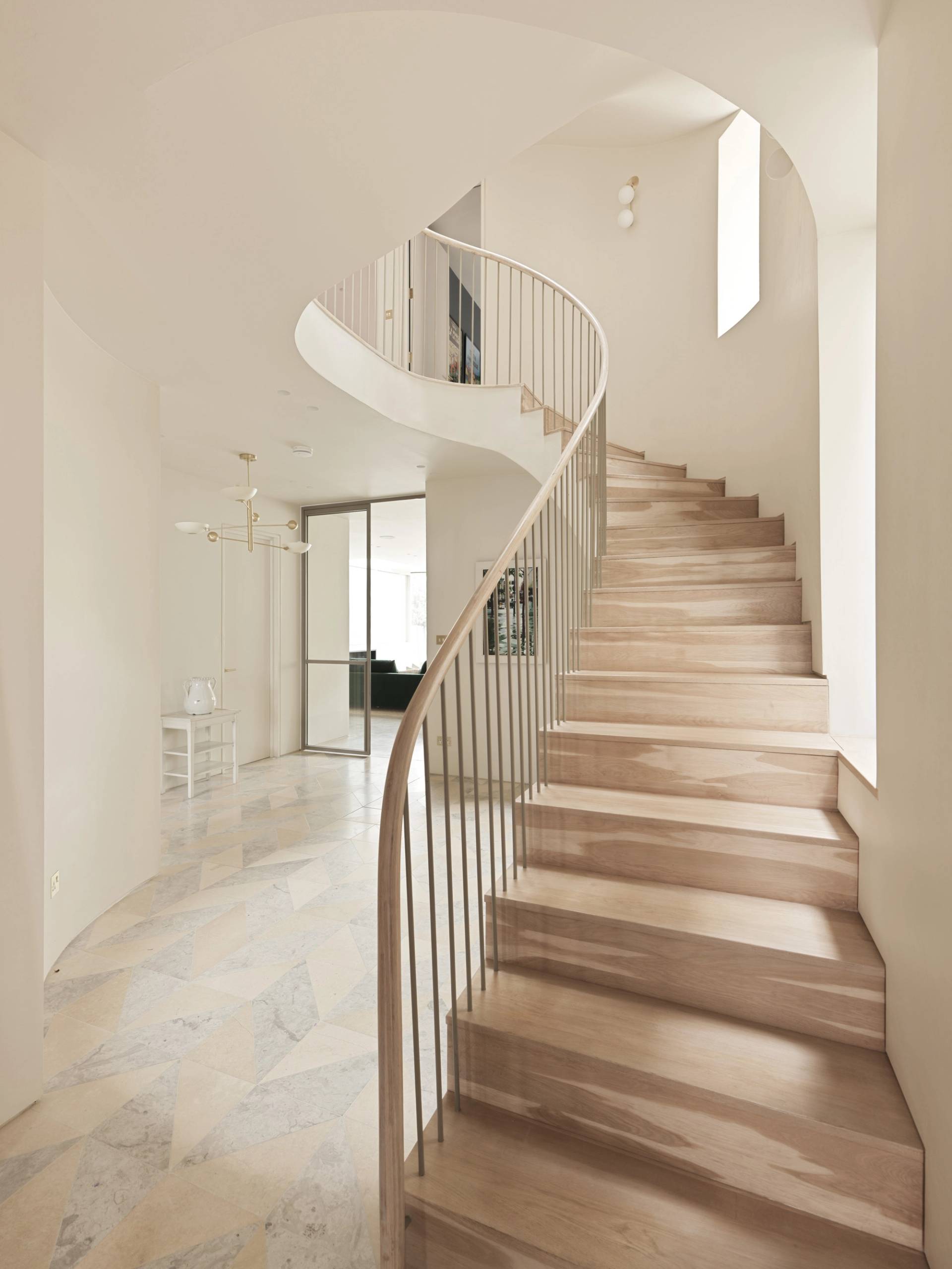 Sculptural spiral staircase featuring timber treads, slim metal balustrades, and curved plaster walls via Love Locations.