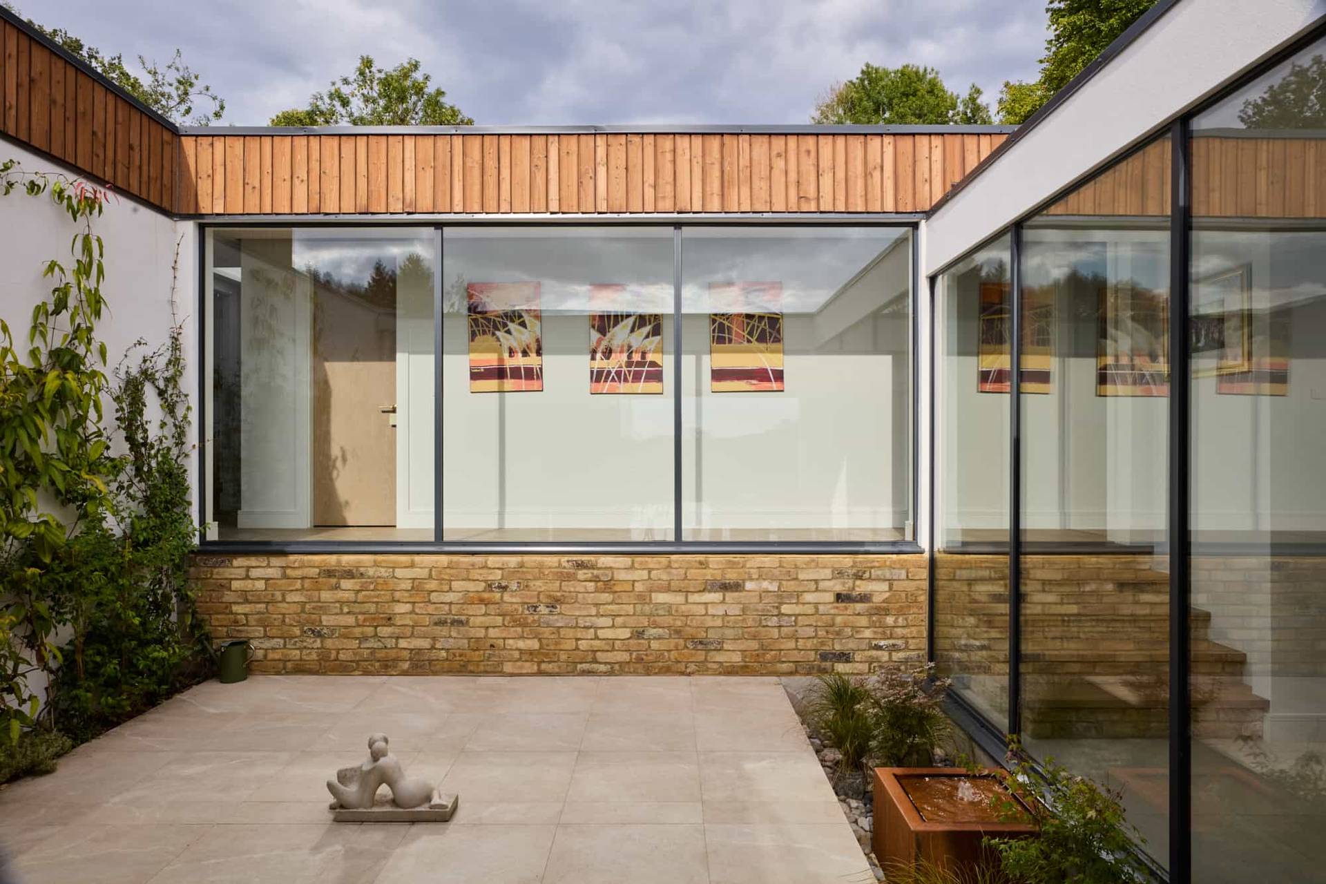 Elevated perspective looking into an enclosed internal glass courtyard with a modern stone sculpture, Love Locations.