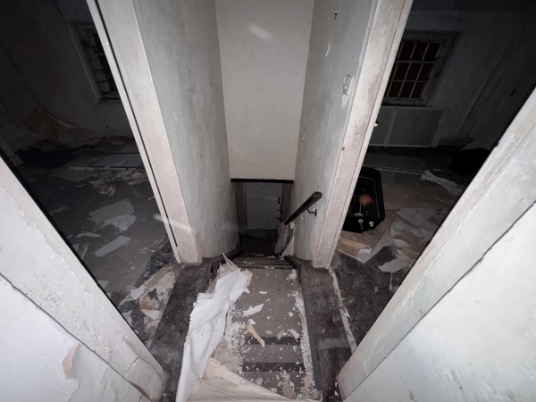 Dismal view looking down a steep, narrow wooden staircase with peeling white walls inside a derelict house, Love Locations SE1.