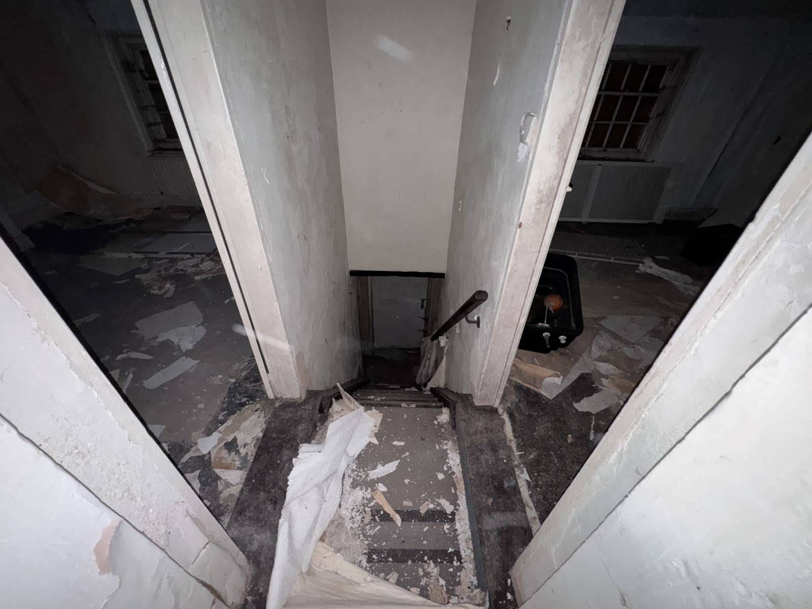 Dismal view looking down a steep, narrow wooden staircase with peeling white walls inside a derelict house, Love Locations SE1.