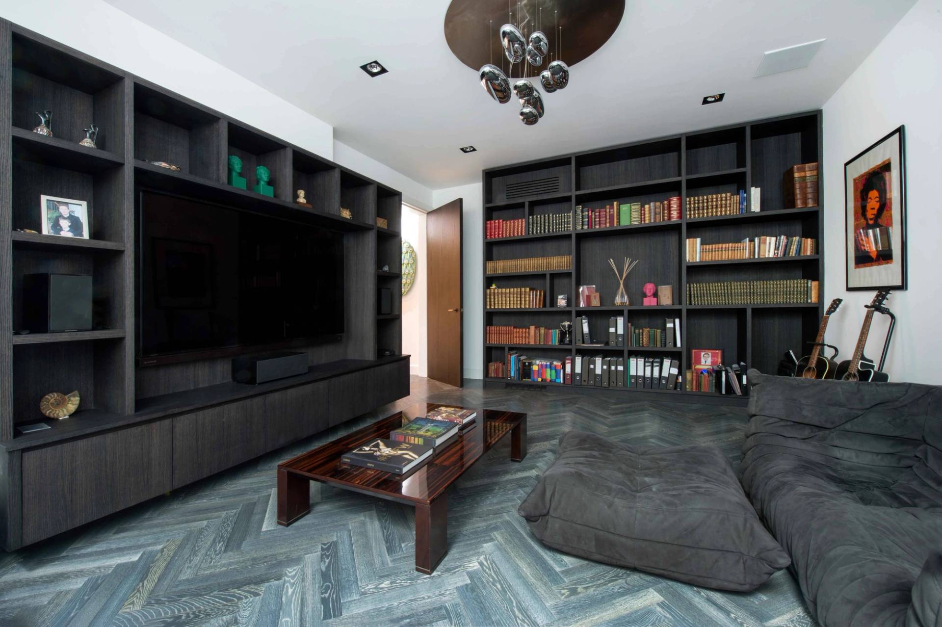 Informal media lounge featuring a comfortable floor cushion setup, dark wood media unit, and herringbone parquet floors, Love Locations NW3.