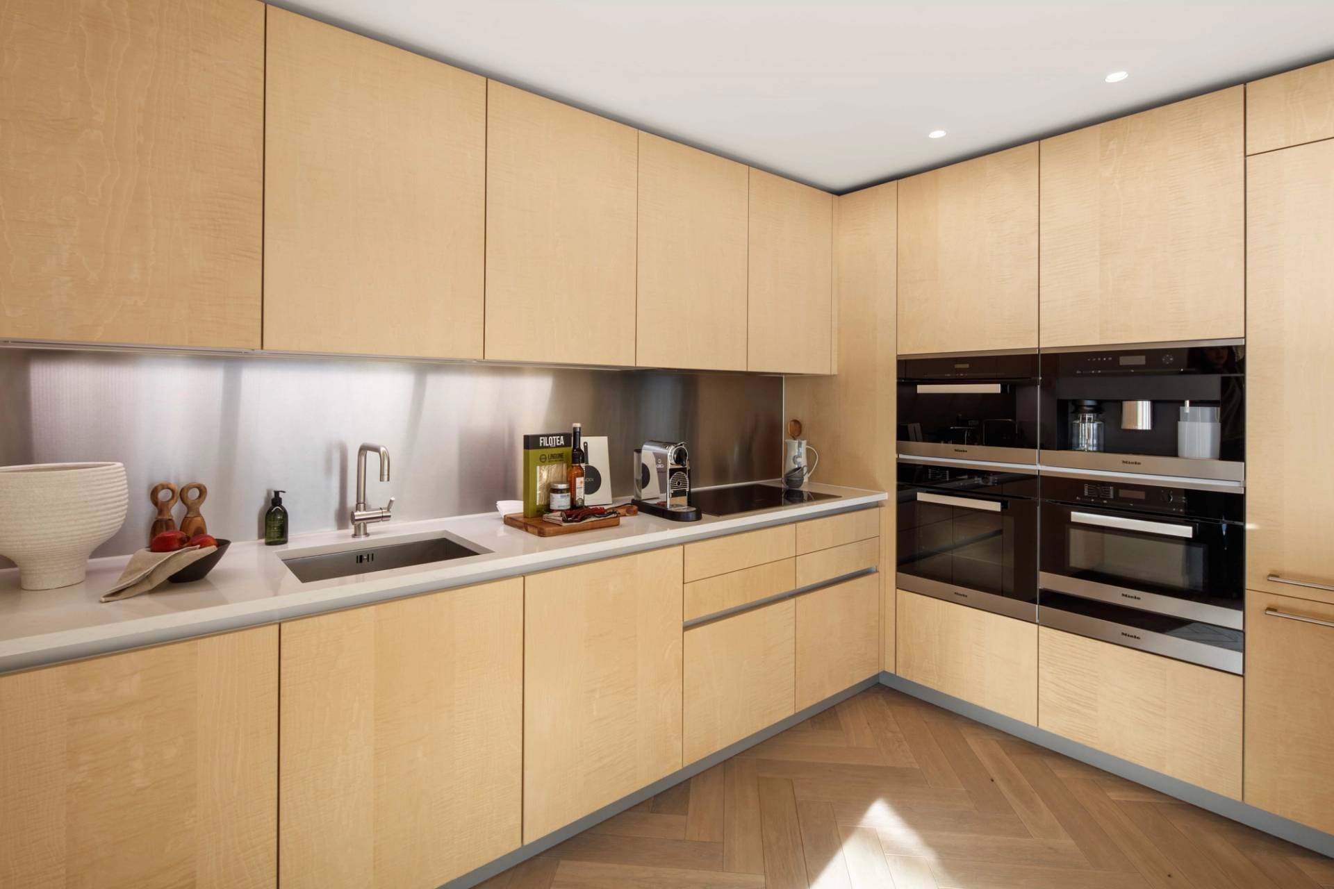 Close-up of minimalist light oak kitchen cabinets and integrated wall ovens in a high-rise EC2A penthouse location, Love Locations.