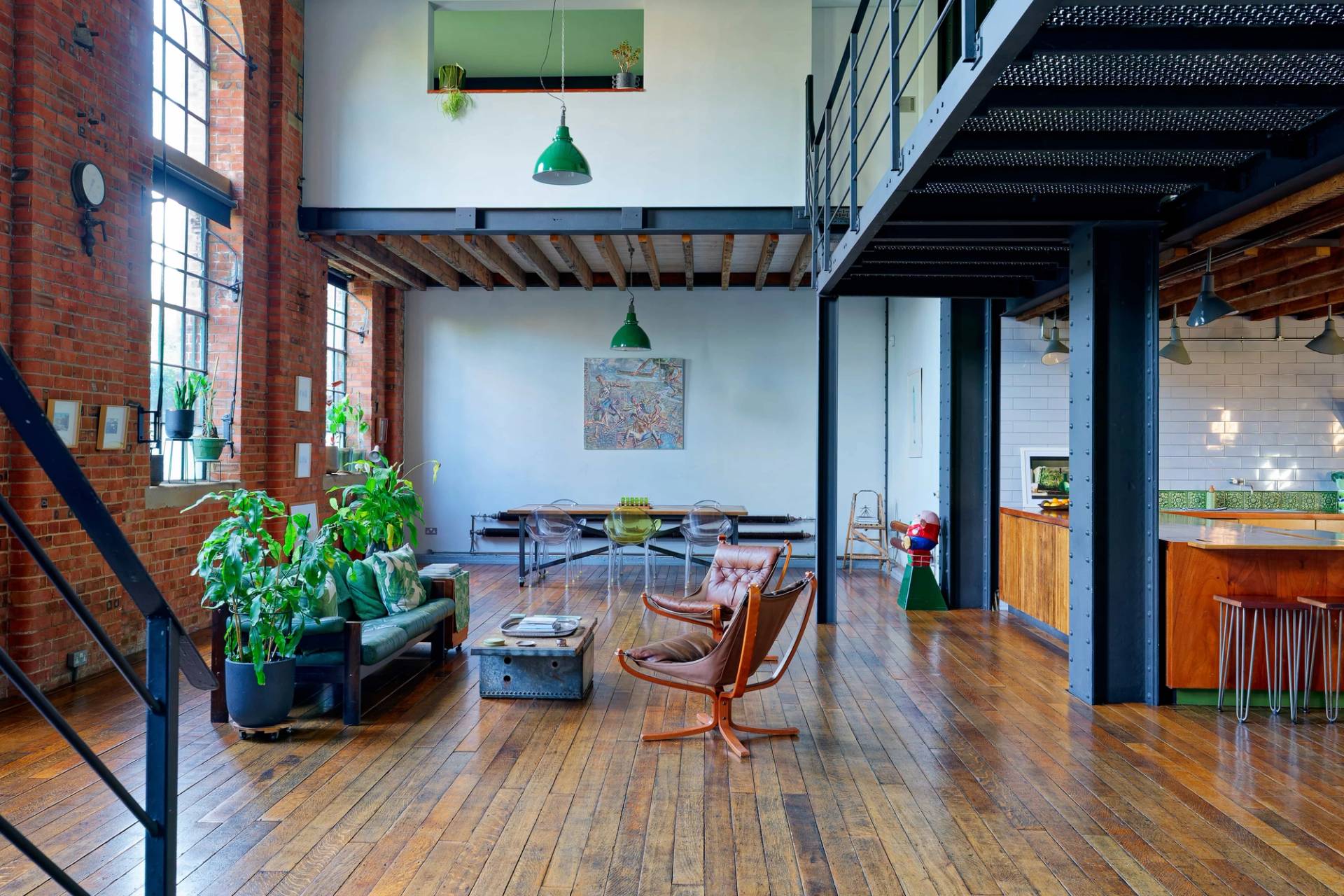 Spacious loft living room in East London with double-height steel frame mezzanine, vintage leather chairs, and dark wood floorboards, Love Locations E14.