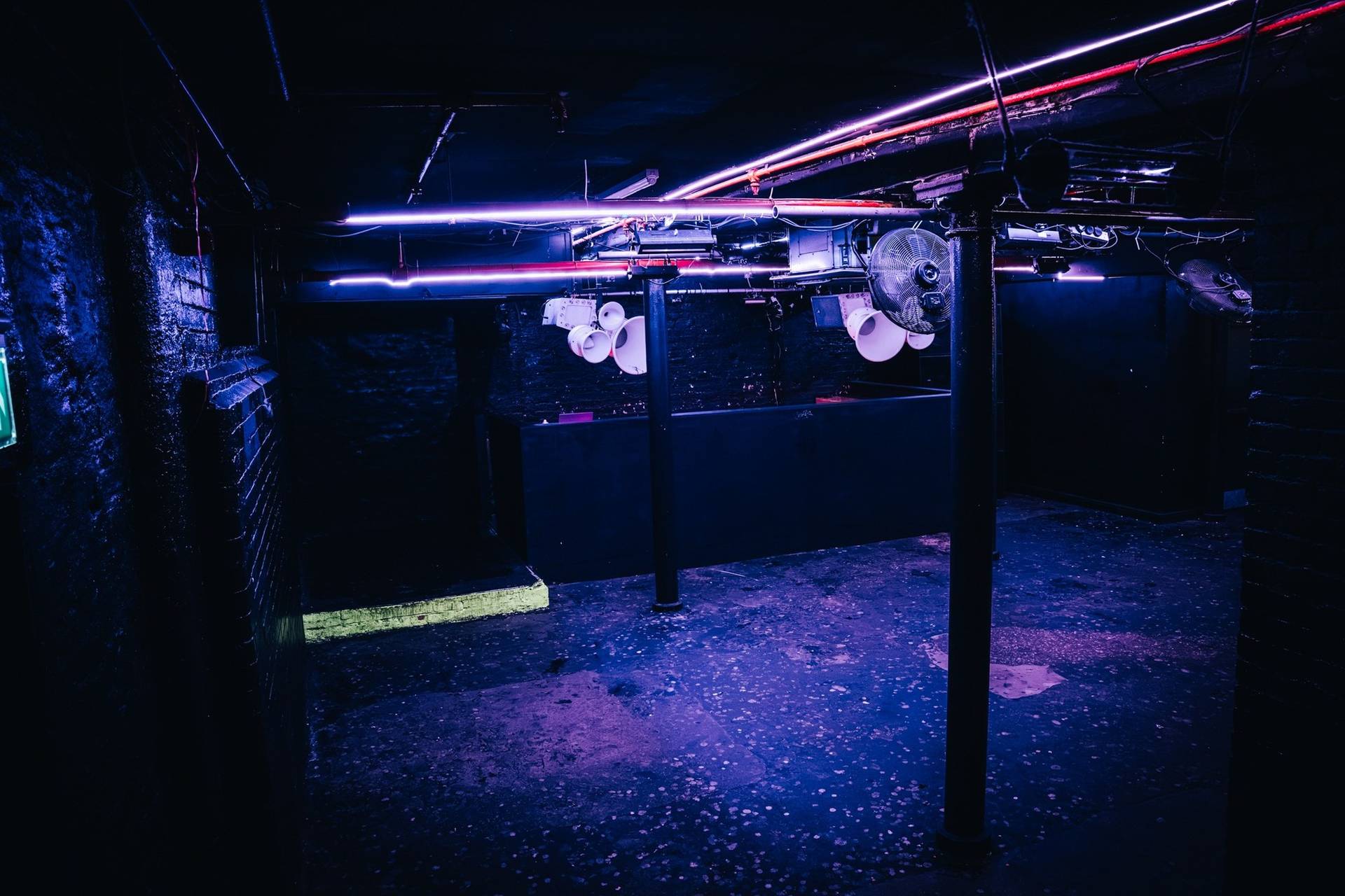 Low-ceiling club floor illuminated with dark purple strip lights and industrial ductwork in Cheetham Hill through Love Locations.