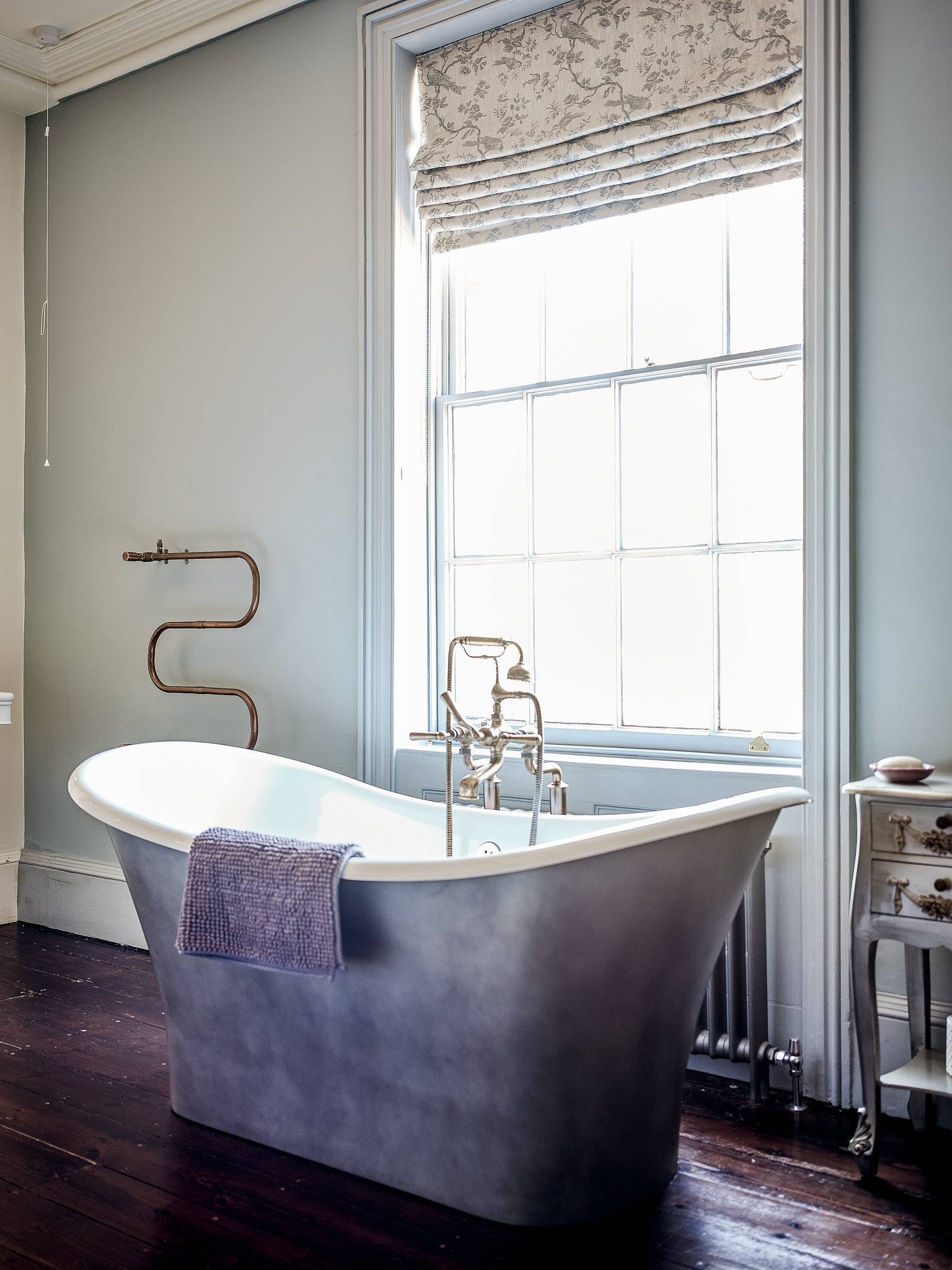 Silver metallic roll-top bath set before a sash window in a light grey bathroom suite, Love Locations.
