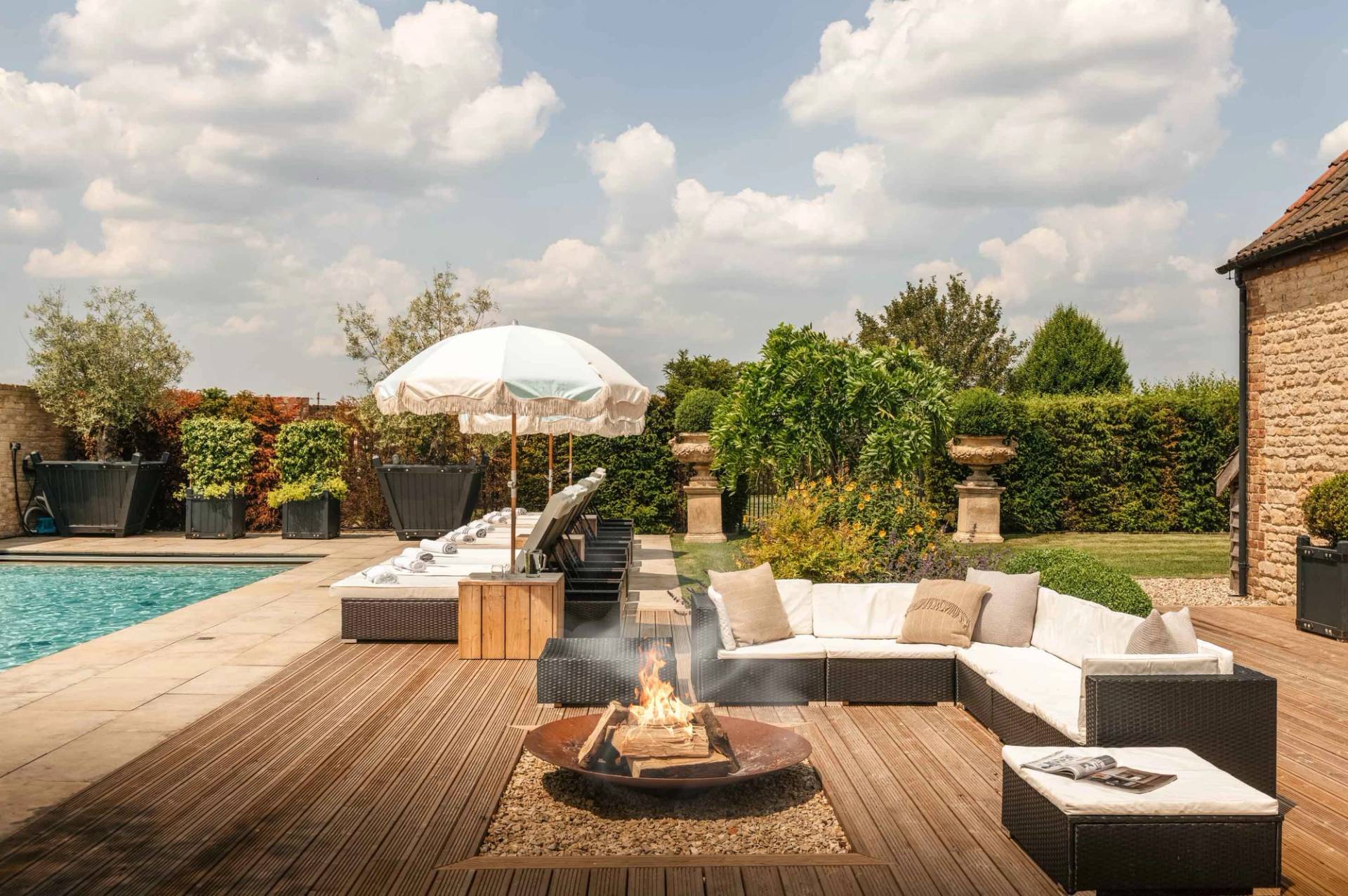 Outdoor lounge and sun terrace with a central metal fire pit and fringed parasol in Cheltenham GL51 from Love Locations.