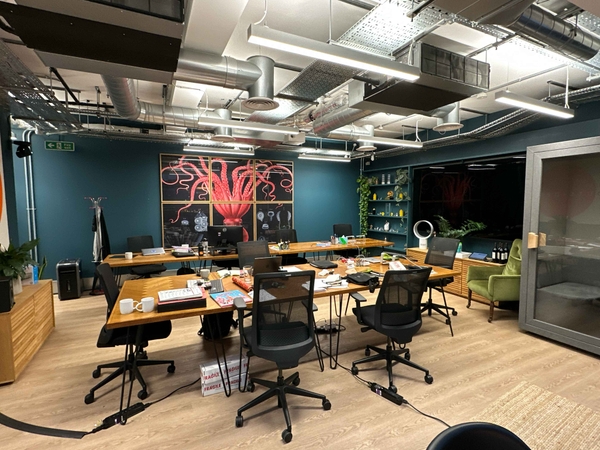 Boardroom or meeting space with a large wooden table, black office chairs, inky blue feature wall with modern bright artwork, and industrial-style exposed ceiling with hanging lights.