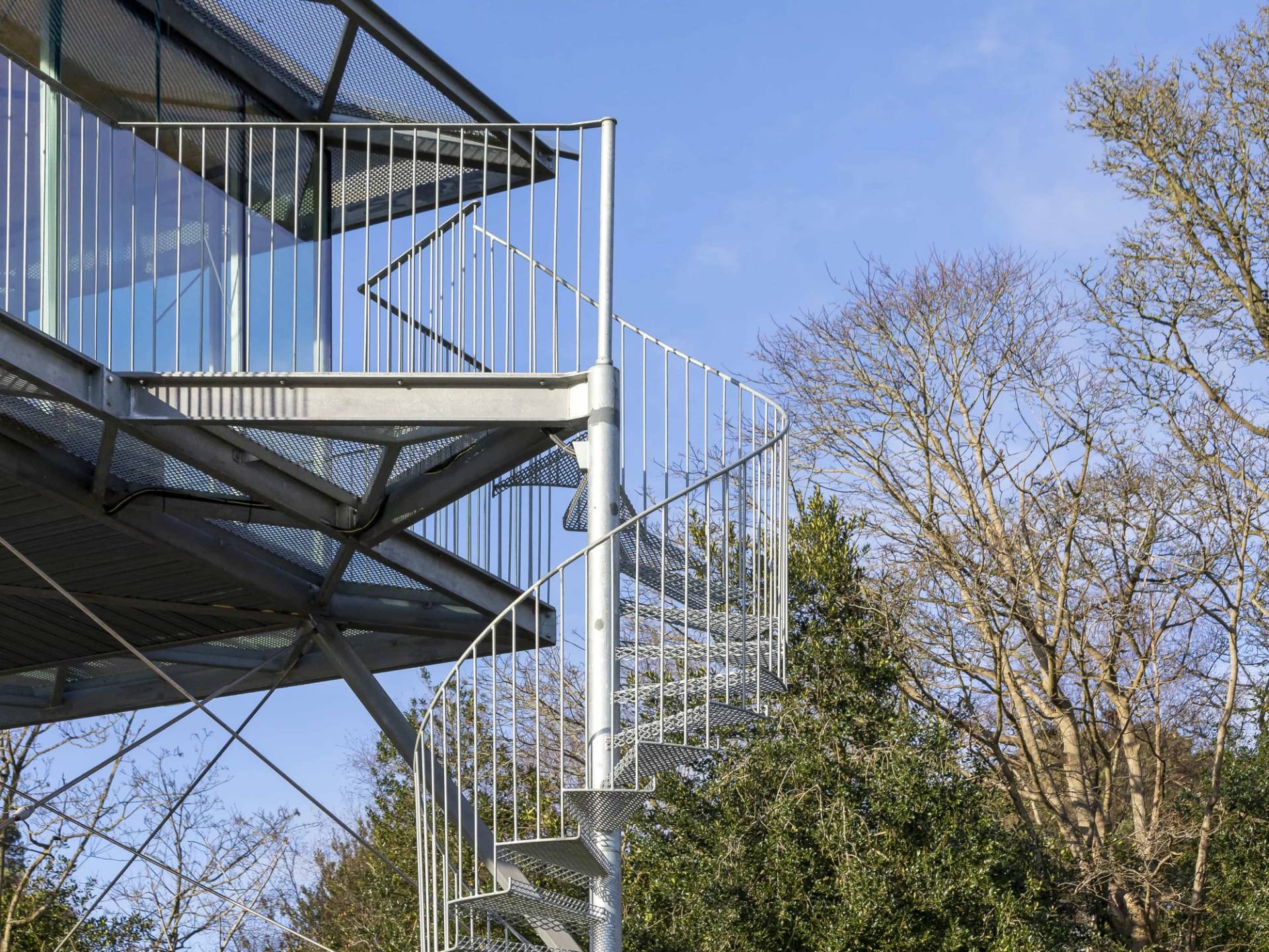 Spiral metal staircase leading up to an elevated glass lookout studio box set against blue skies, Love Locations IP17.