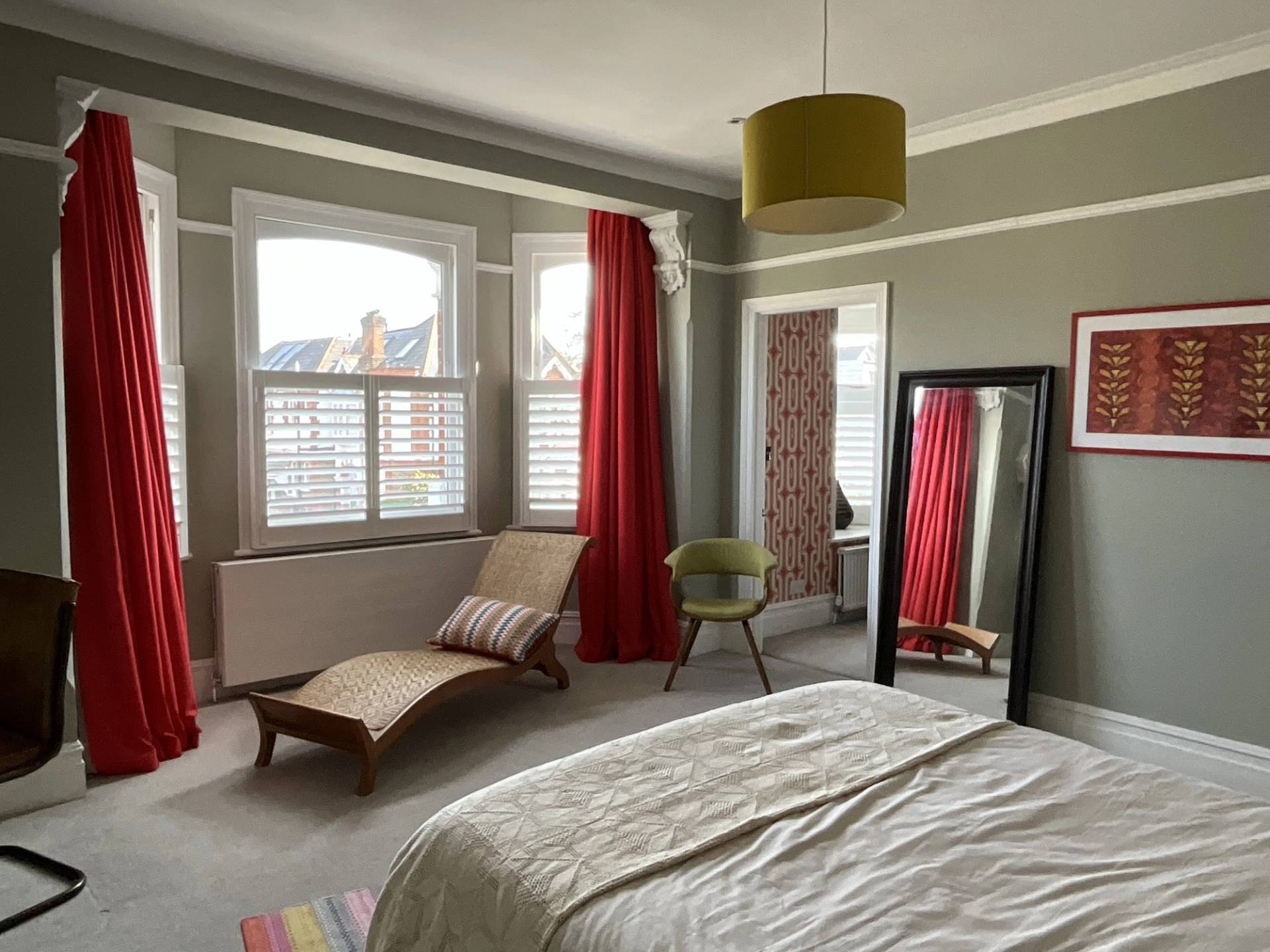 Sunlit bedroom corner with red drapes, chaise lounge, and view toward an ensuite bathroom transition, Love Locations W3.