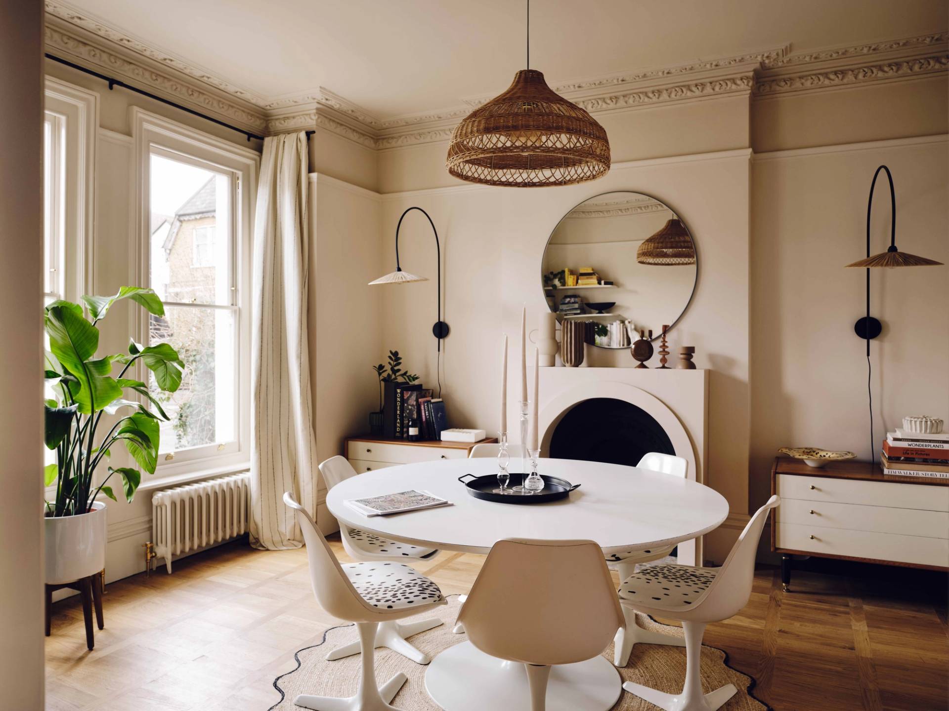Off-white dining room featuring a round white dining table, modern bucket chairs, arched fireplace, and wicker pendant light, Love Locations CR0.