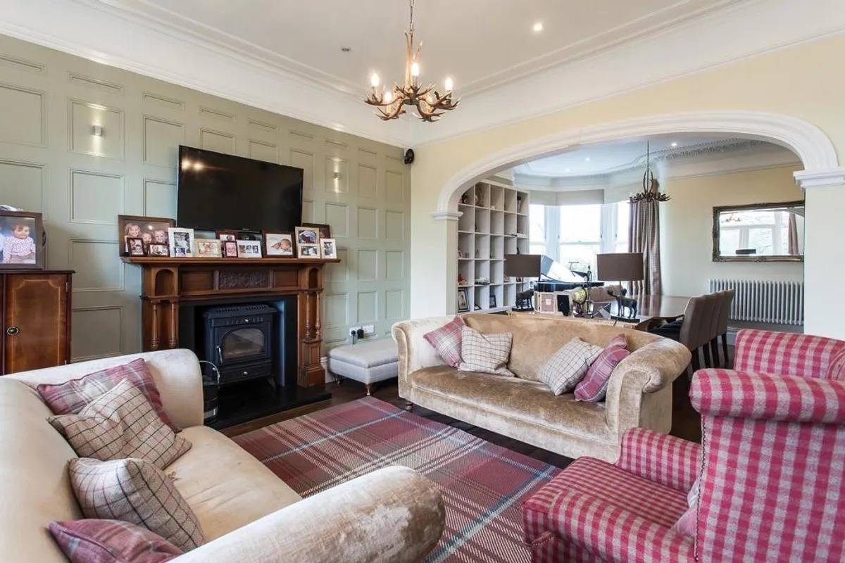 Period sitting room photoshoot location in Stockport SK6 via Love Locations, showcasing a classic dark wood mantelpiece, cast iron fireplace, and tartan carpet.