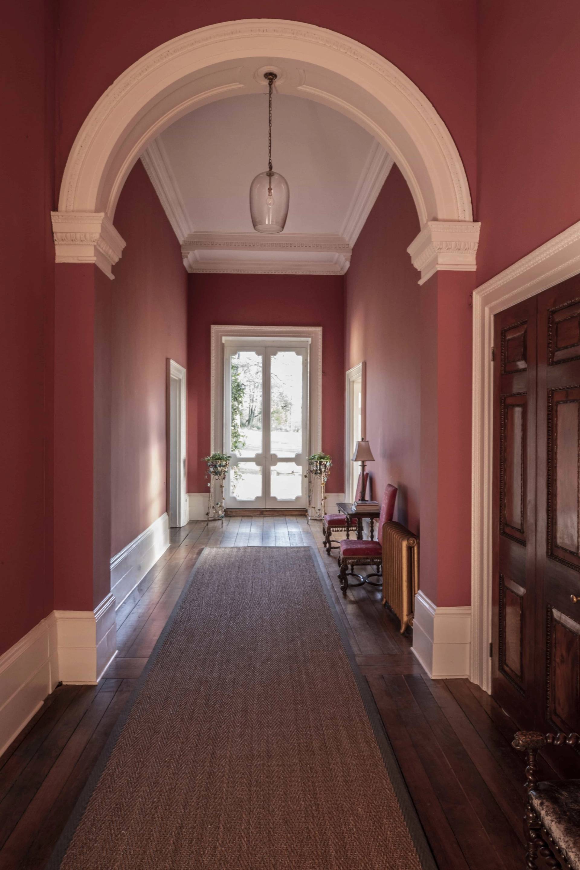 Terracotta red corridor looking towards double glass doors framed by architectural arches in a Tugby location house, Love Locations LE7.