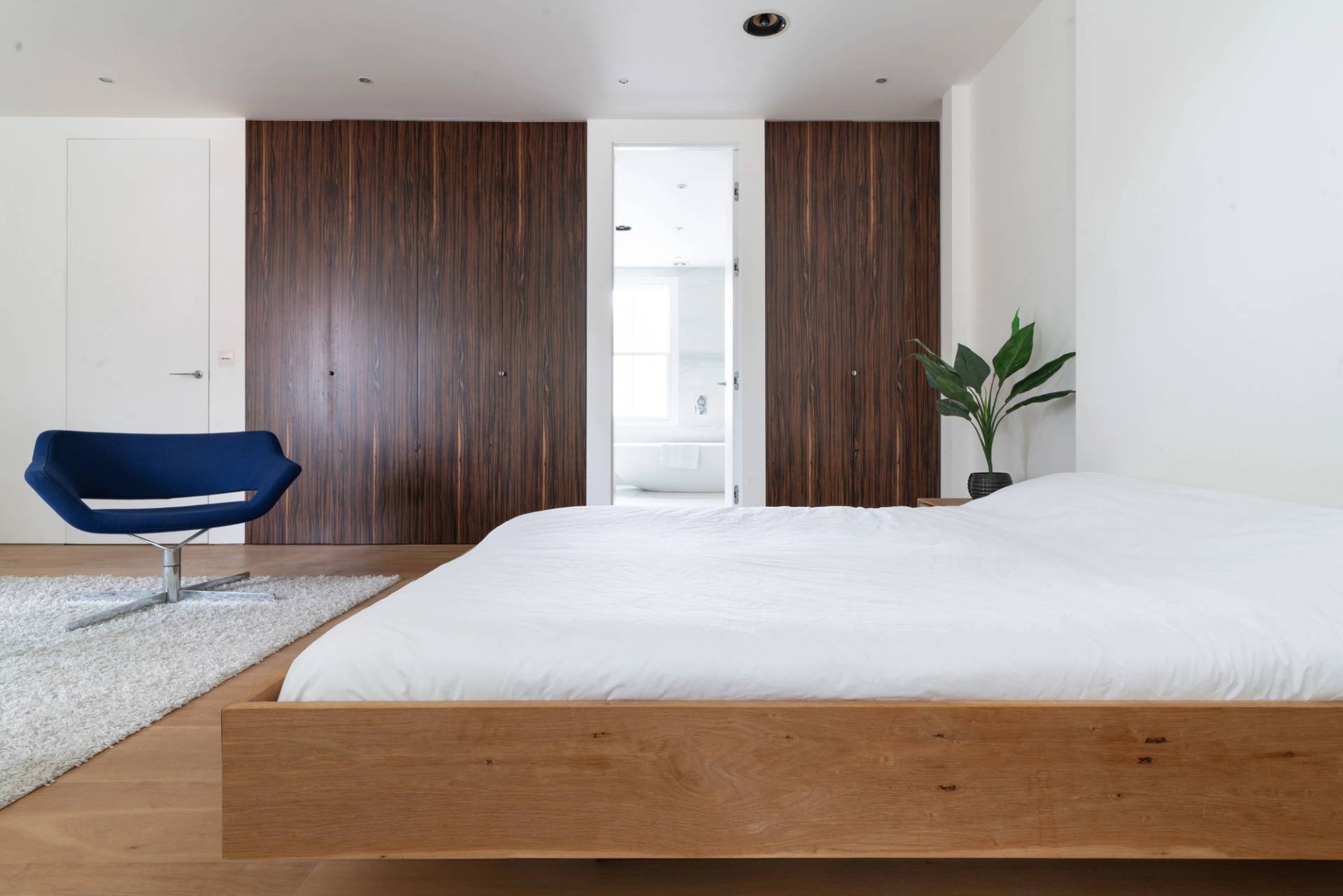 Contemporary living room alcove with blue armchair seating, glass coffee table, and wood floors, Love Locations SW6.