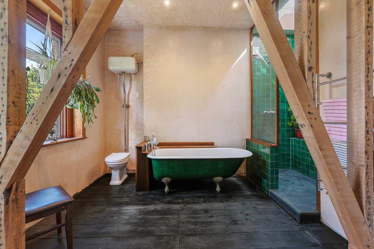 Spacious bathroom featuring exposed timber A-frame beams, green roll-top bath, and dark timber floors, ideal for wellness product shoots, Love Locations E7.