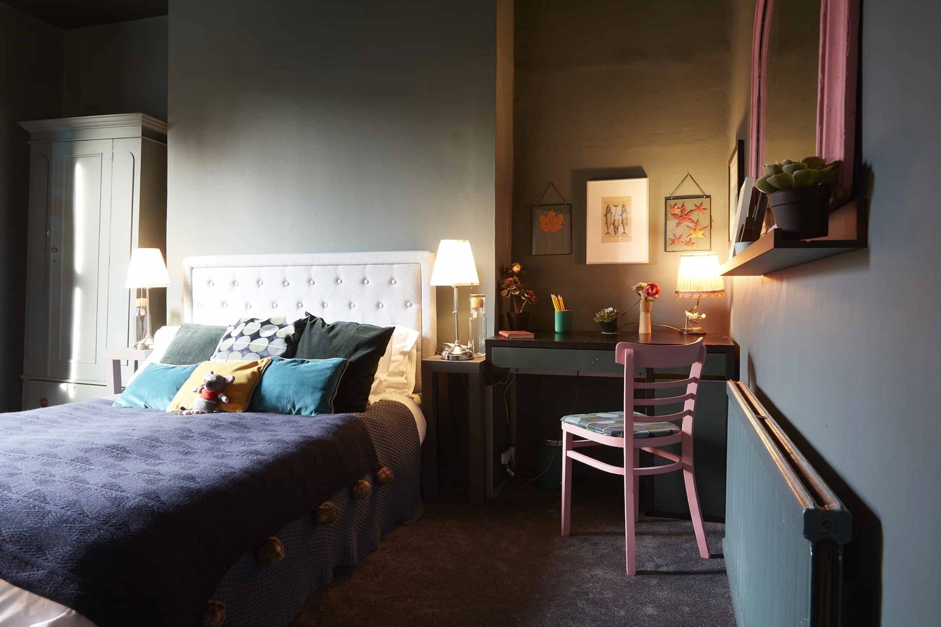 Moody dark teal guest bedroom featuring a white button-tufted headboard, desk nook, and pink accent chair, Love Locations N5.