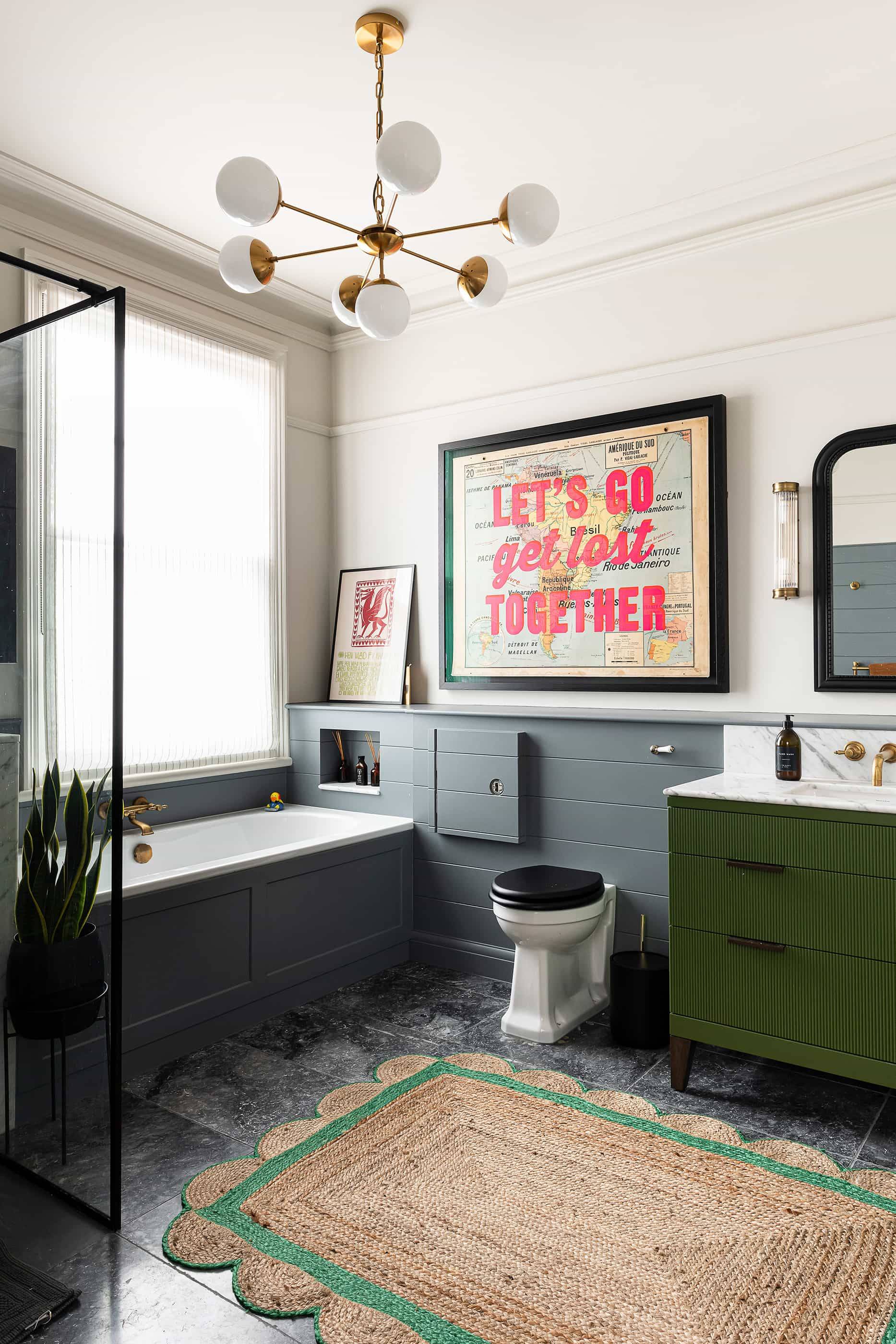 Ensuite bathroom with dark grey wall panelling, dark green vanity, brass taps, and statement artwork, Love Locations.