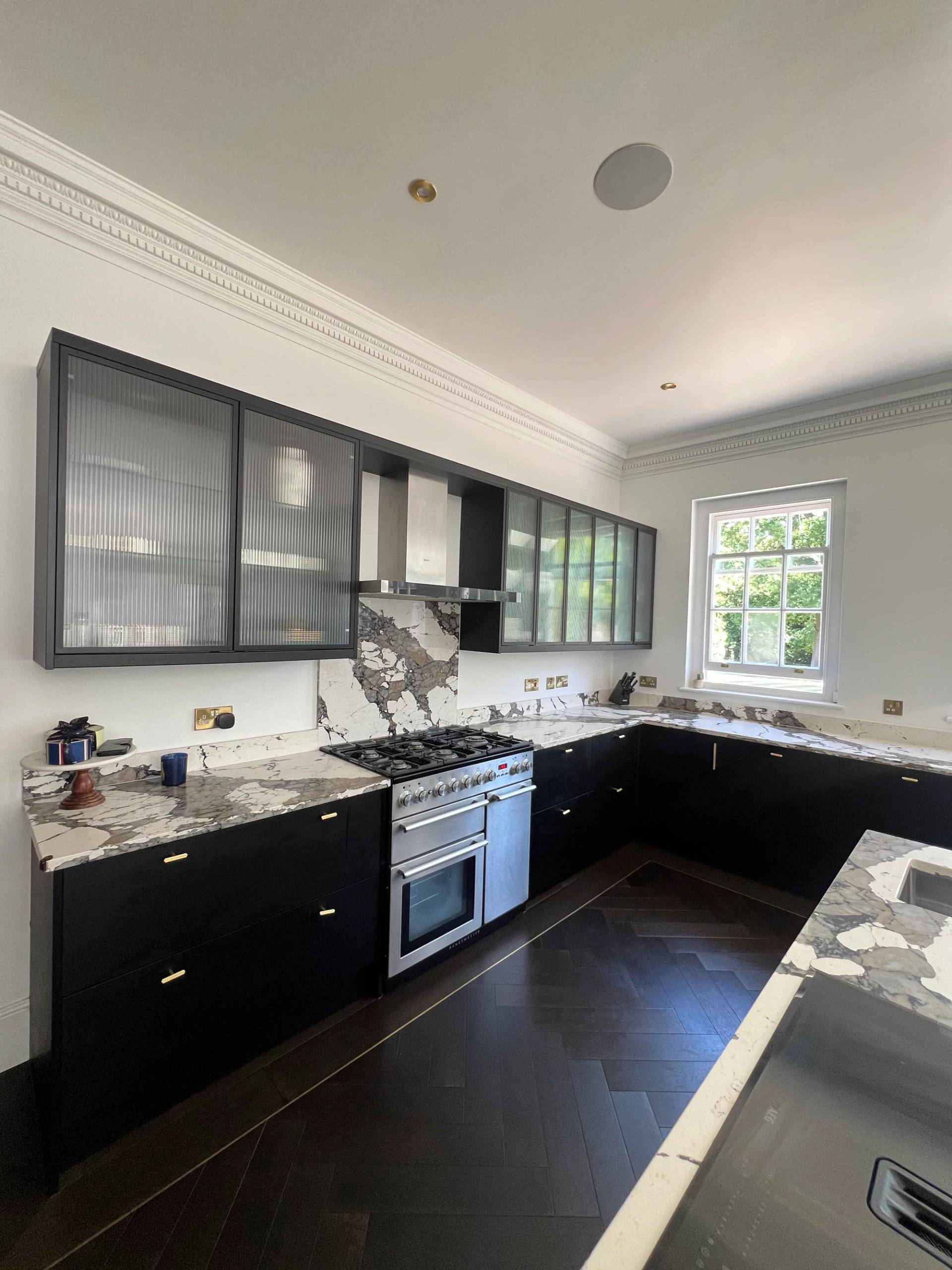 Contemporary luxury kitchen in Bromley, BR7 featuring black shaker cabinets, stainless steel range cooker, and dark parquet flooring, Love Locations.