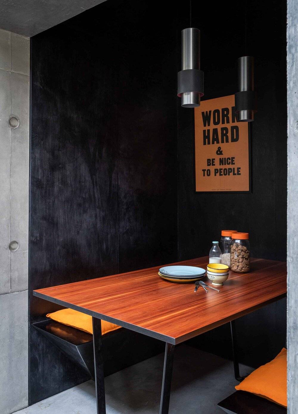 Cozy dining alcove with dark concrete walls, rich timber table, and yellow poster art, ideal for food ads, Love Locations BN7.