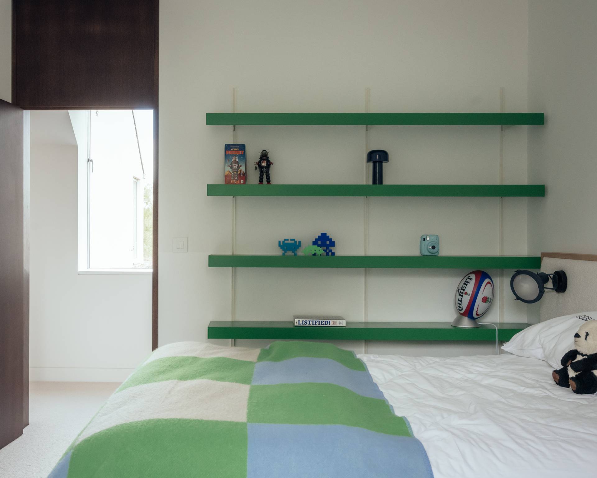 Playful children's or guest bedroom featuring vibrant green wall shelving and a modern patterned quilt, suitable for youthful lifestyle shoots, Love Locations SO20.