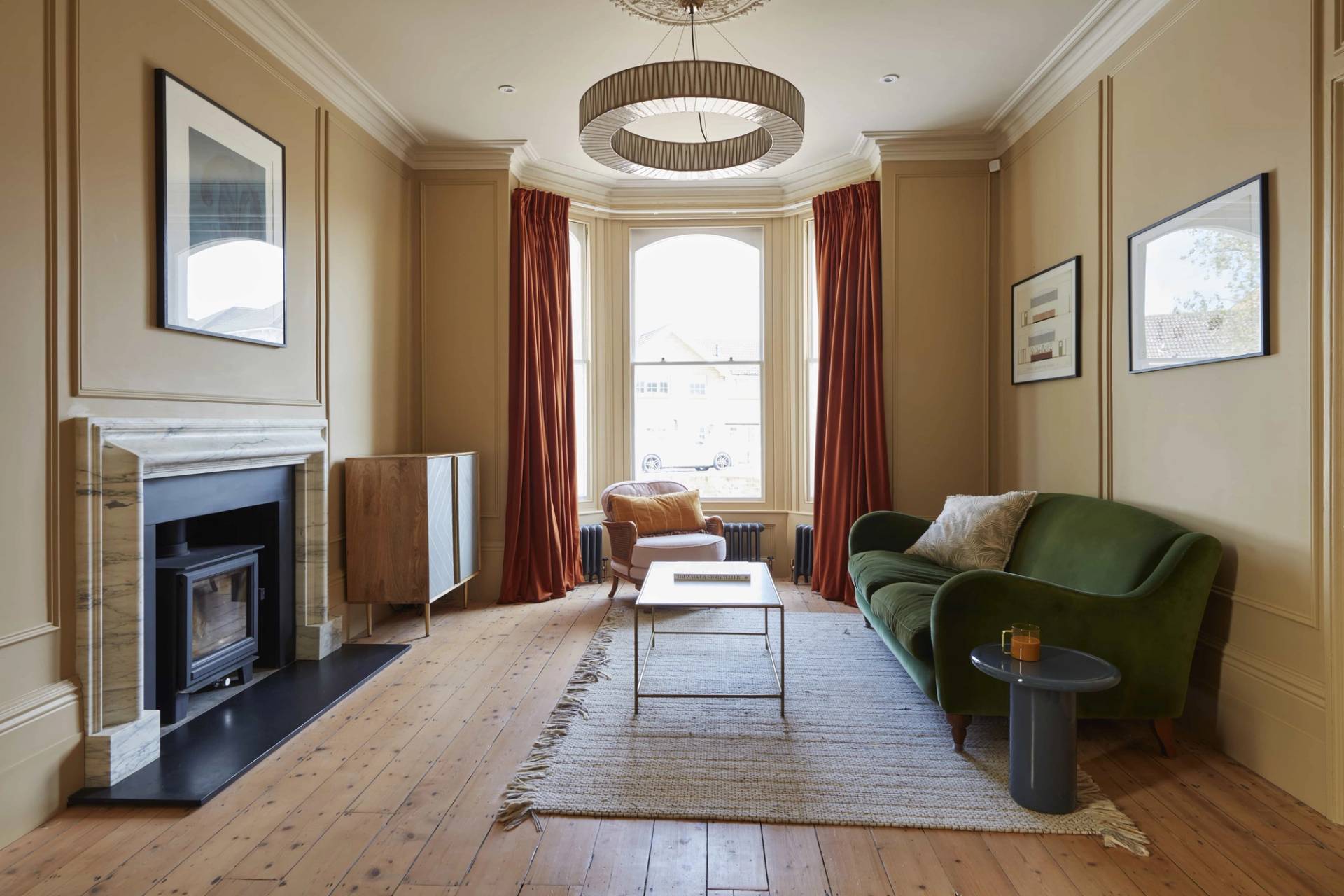 Warm ochre living room featuring a double bay window, green sofa, terracotta curtains, and original fireplace, ideal for domestic brand filming, Love Locations TN34.