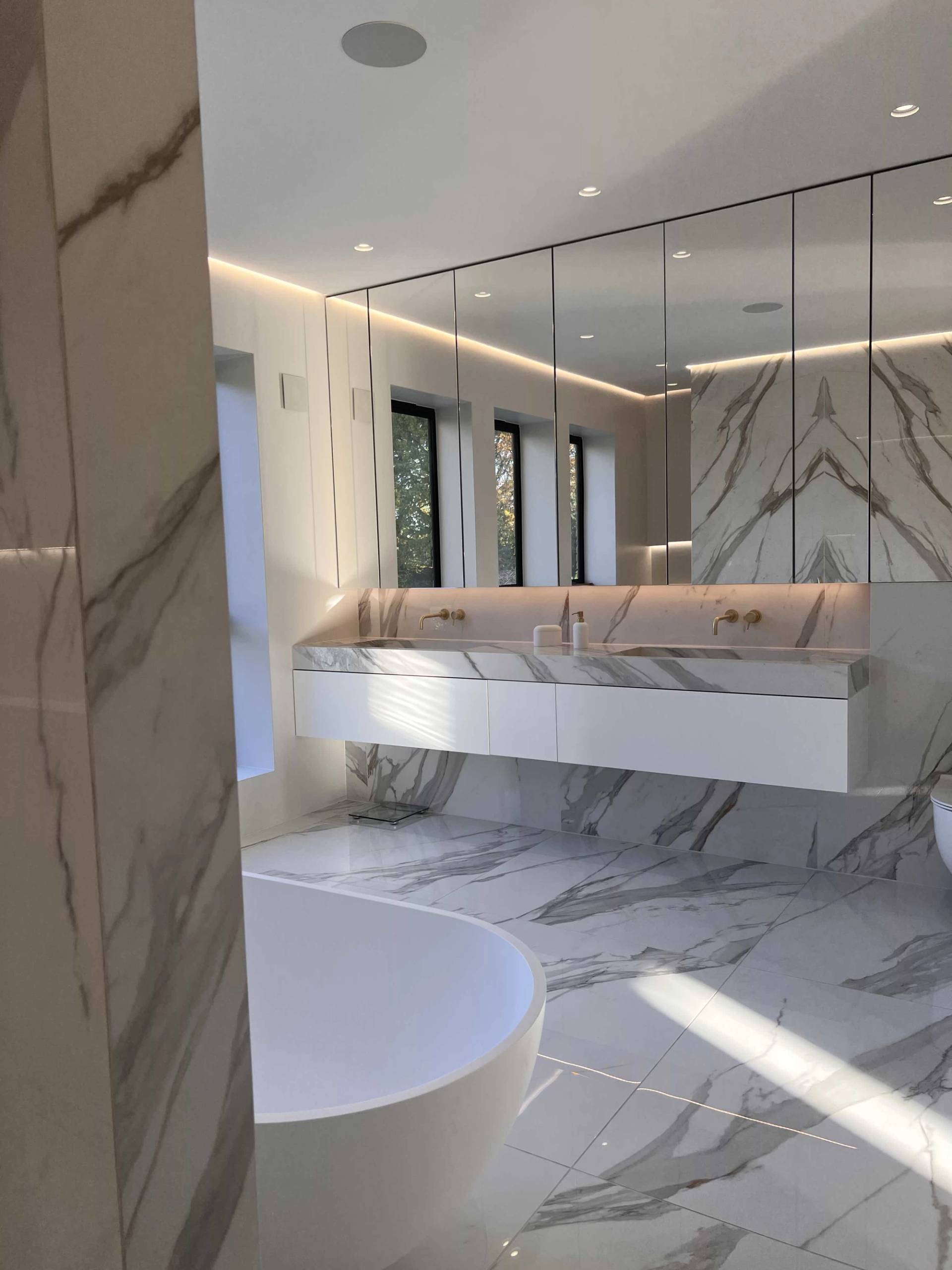 Calacatta marble bathroom suite featuring double basin vanities, brass taps, and integrated LED strip lighting, Love Locations.