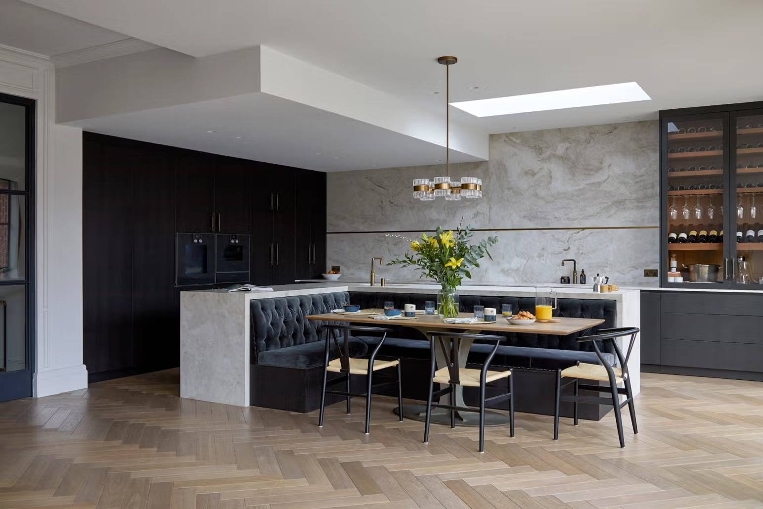 Modern Victorian home extension in Teddington, TW11 featuring a marble kitchen island, dark banquette seating, and herringbone oak floors via Love Locations.