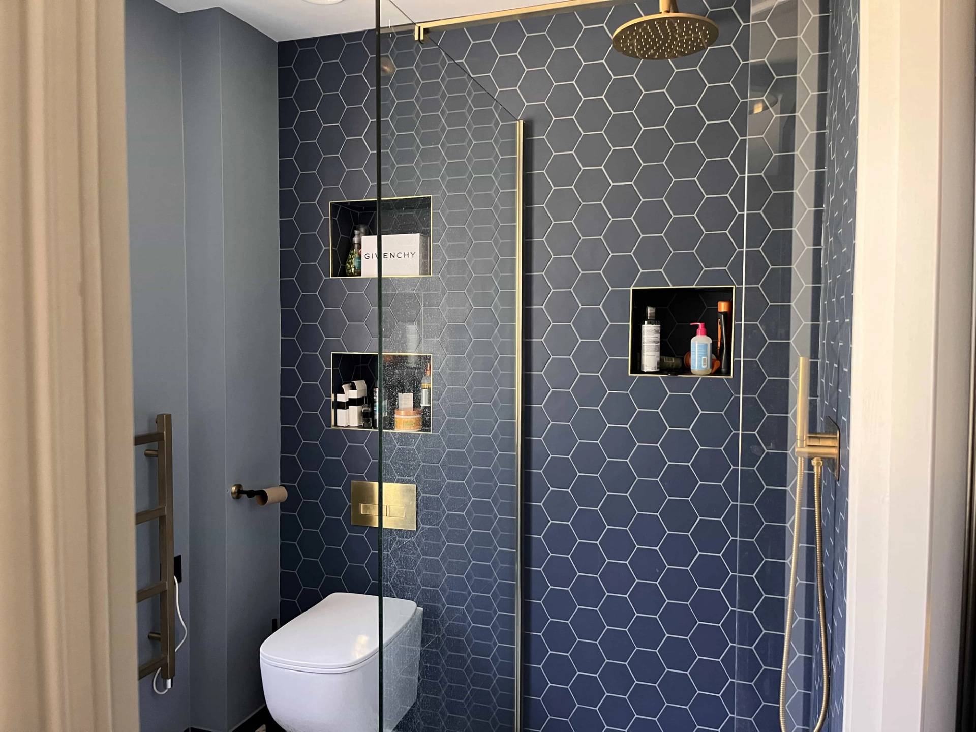 Dark navy blue tile bathroom featuring dark hexagon tiles, gold shower fittings, and recessed wall niches, Love Locations GU3.