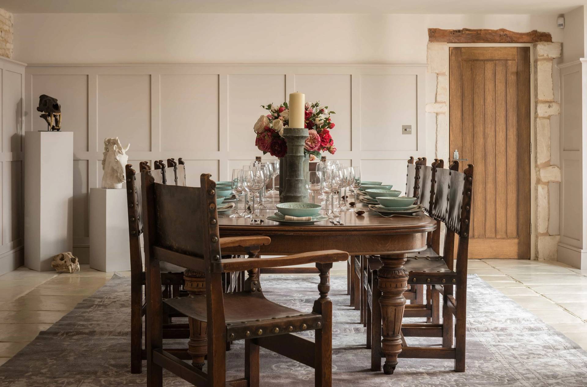 Grand rustic dining room location house in Cheltenham GL51 through Love Locations, featuring a heavy wooden dining table, carved high-back chairs, light wall panelling, and a floral centerpiece.