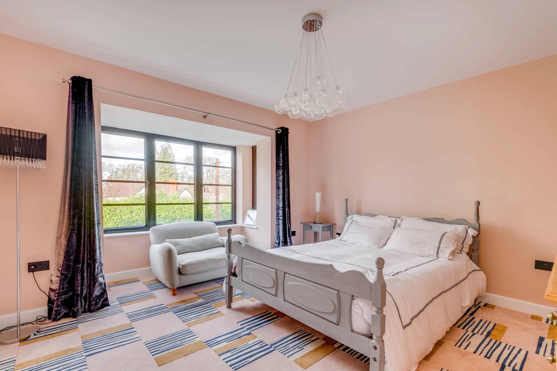 Pastel pink bedroom suite with grey wooden bed frame, large window, and light area rug, Love Locations CB2.