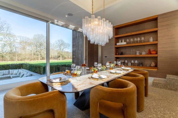 Love Locations architectural property location Surrey: Sunlit dining room looking through massive floor-to-ceiling glass windows onto open green meadows, optimized for daylight film productions.