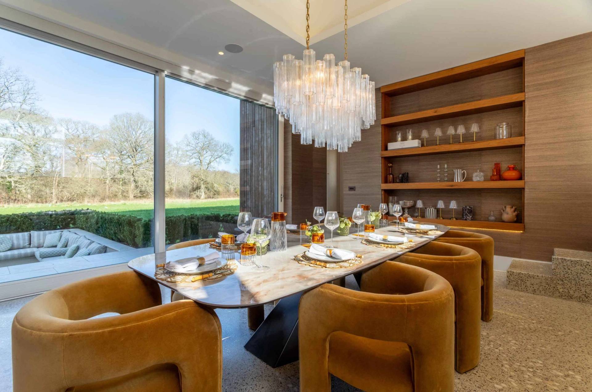 Love Locations architectural property location Surrey: Sunlit dining room looking through massive floor-to-ceiling glass windows onto open green meadows, optimized for daylight film productions.
