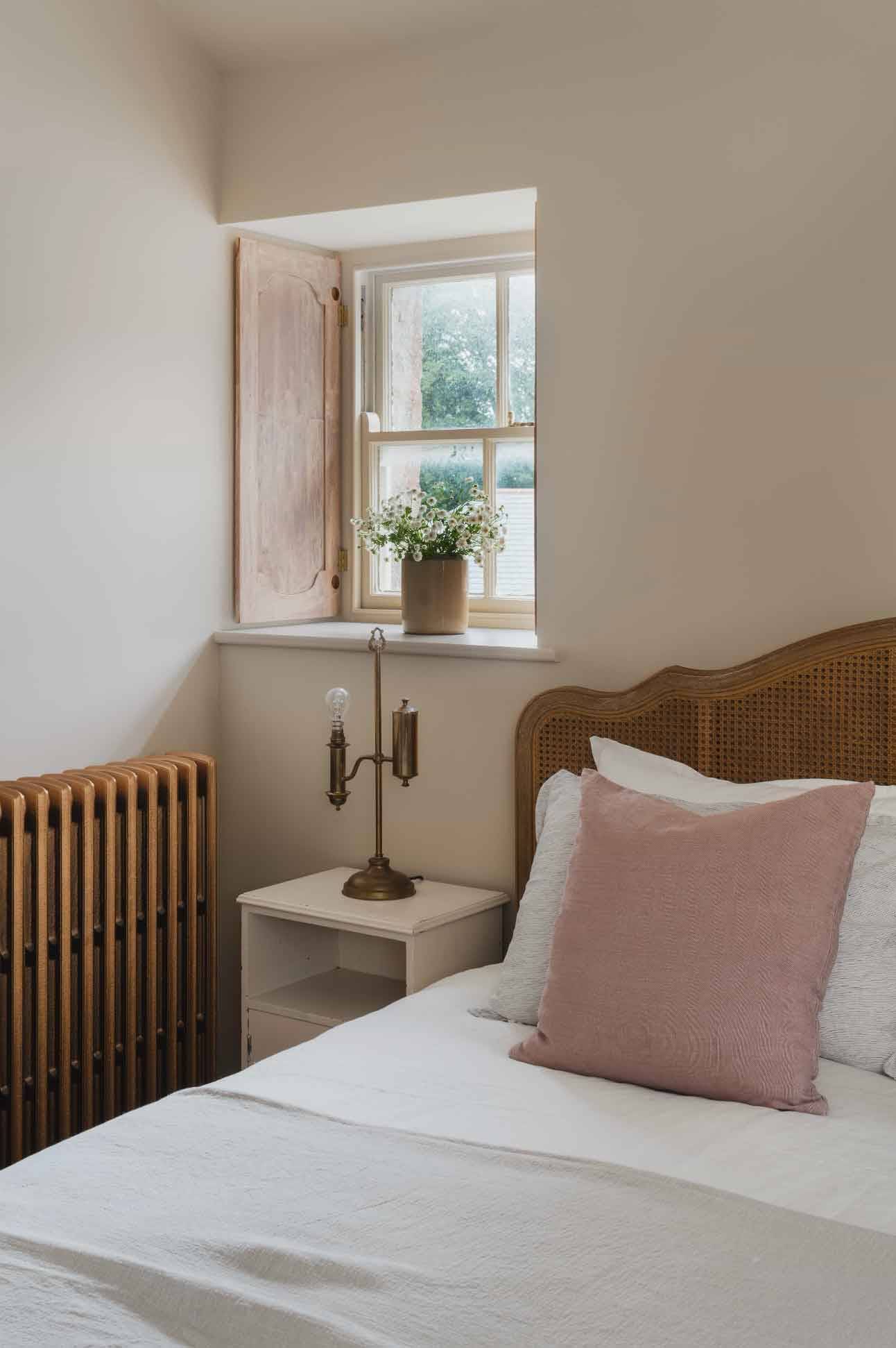 Cozy bedroom detail showing a cane headboard, wooden shutters, and brass candlestick holder via Love Locations.