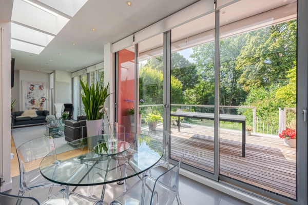 Modern glass dining table and transparent chairs set against large sliding glass doors leading to an outdoor deck, ideal for summer lifestyle campaigns, Love Locations.