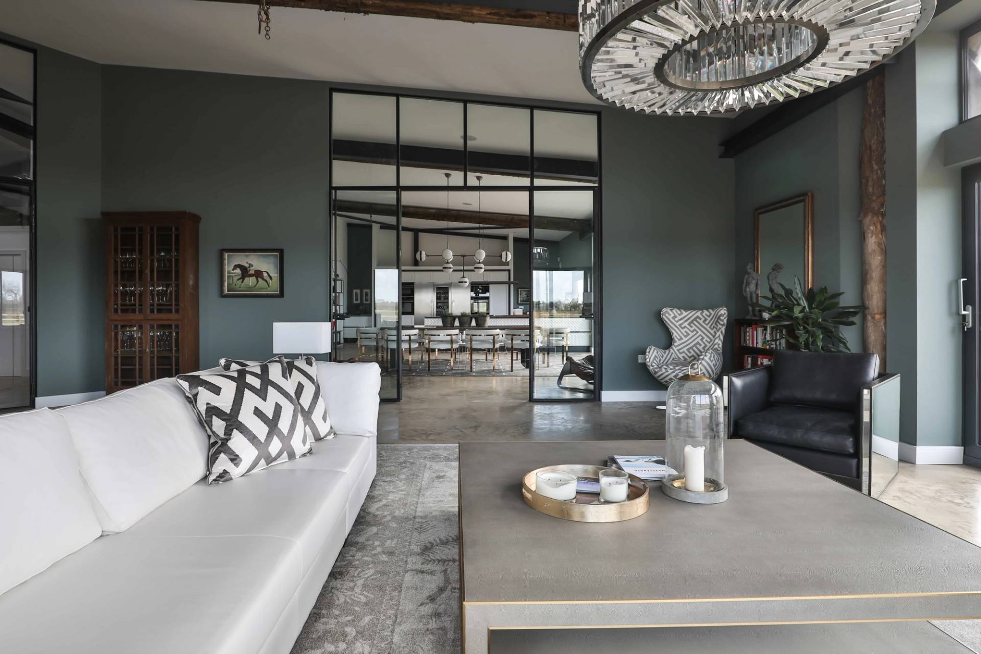 View looking past a plush white sofa and coffee table toward black metal glass framed partition doors, Love Locations CV23.