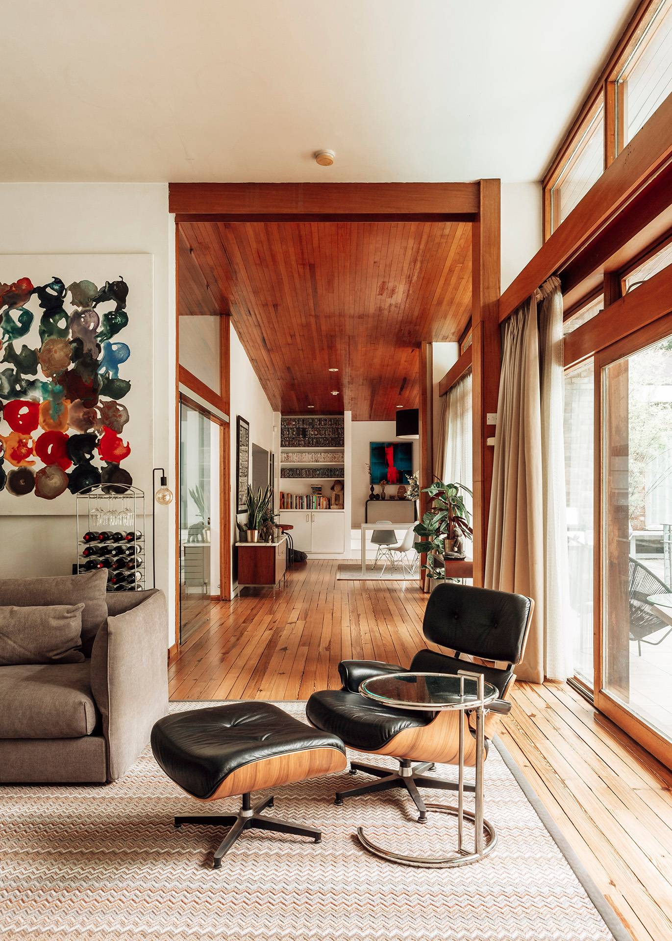 Open-plan living room view showing a classic lounge chair, hardwood flooring, and seamless indoor-outdoor sightlines, Love Locations.