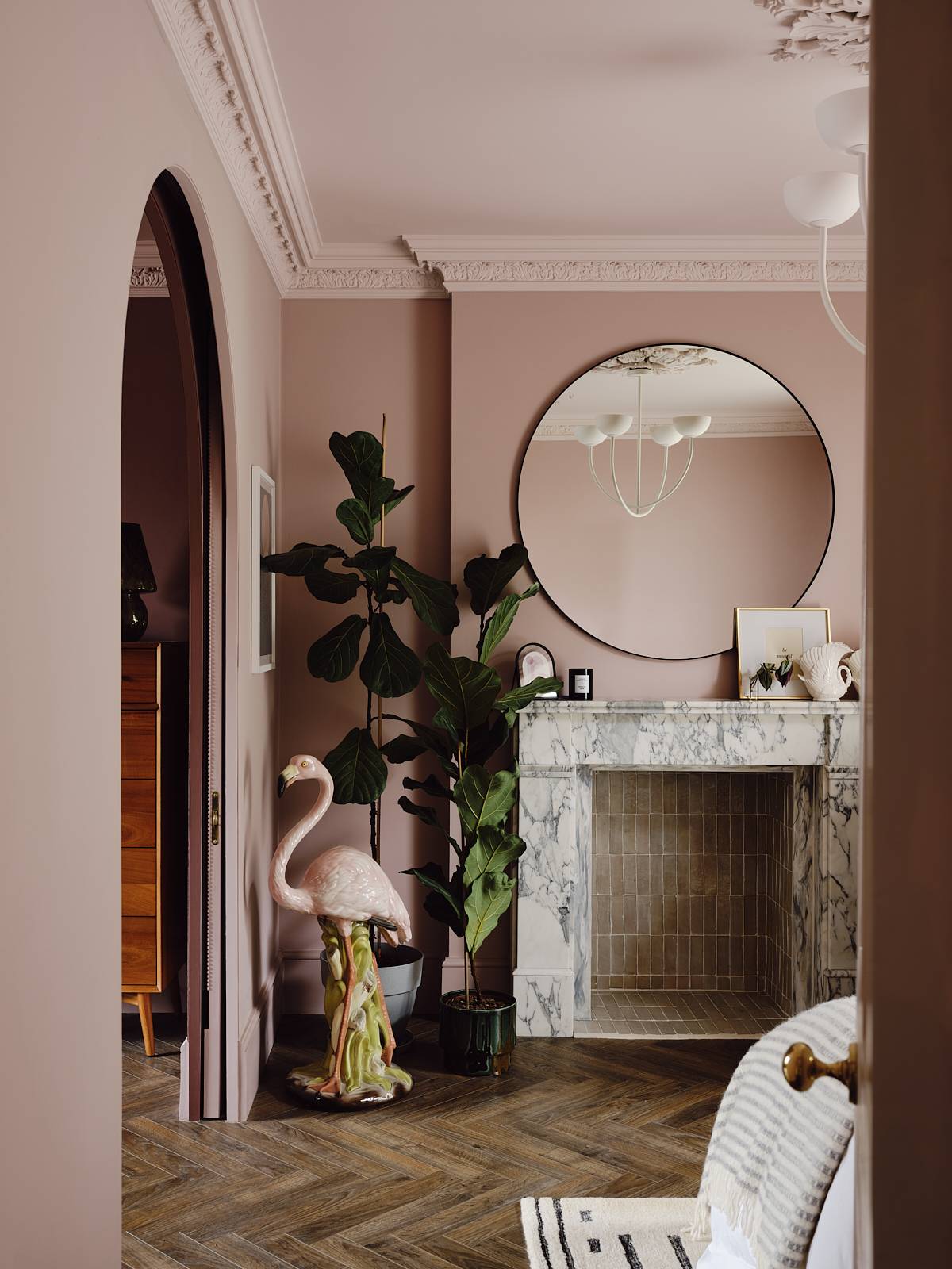 Plaster pink bedroom featuring an ornate grey marble fireplace surround, large round mirror, and vintage flamingo statue, Love Locations CR0.