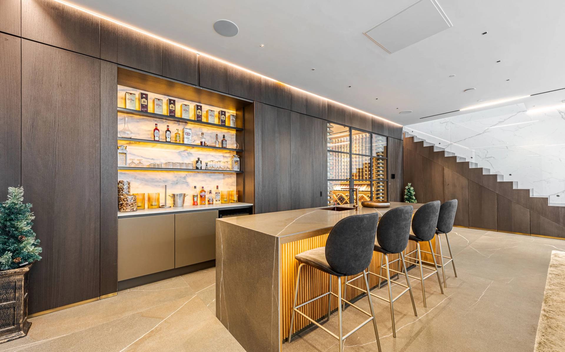 Bespoke basement home bar featuring illuminated brass bottle shelves, marble island, and high bar stools, Love Locations SW11.