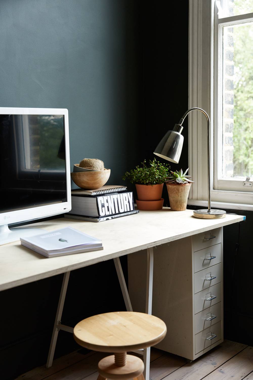 Home office study nook in Palmers Green, N13 featuring dark teal walls, wooden desk, silver desk lamp, and window light, Love Locations.