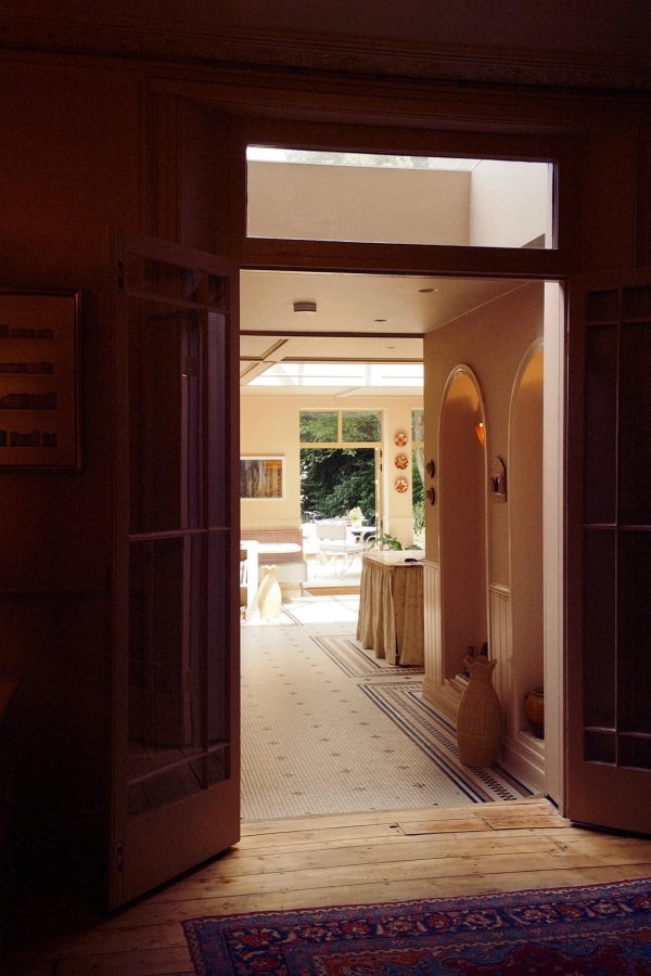 Warmly lit interior view looking through open wooden double doors into a sunlit conservatory filming space, Love Locations.