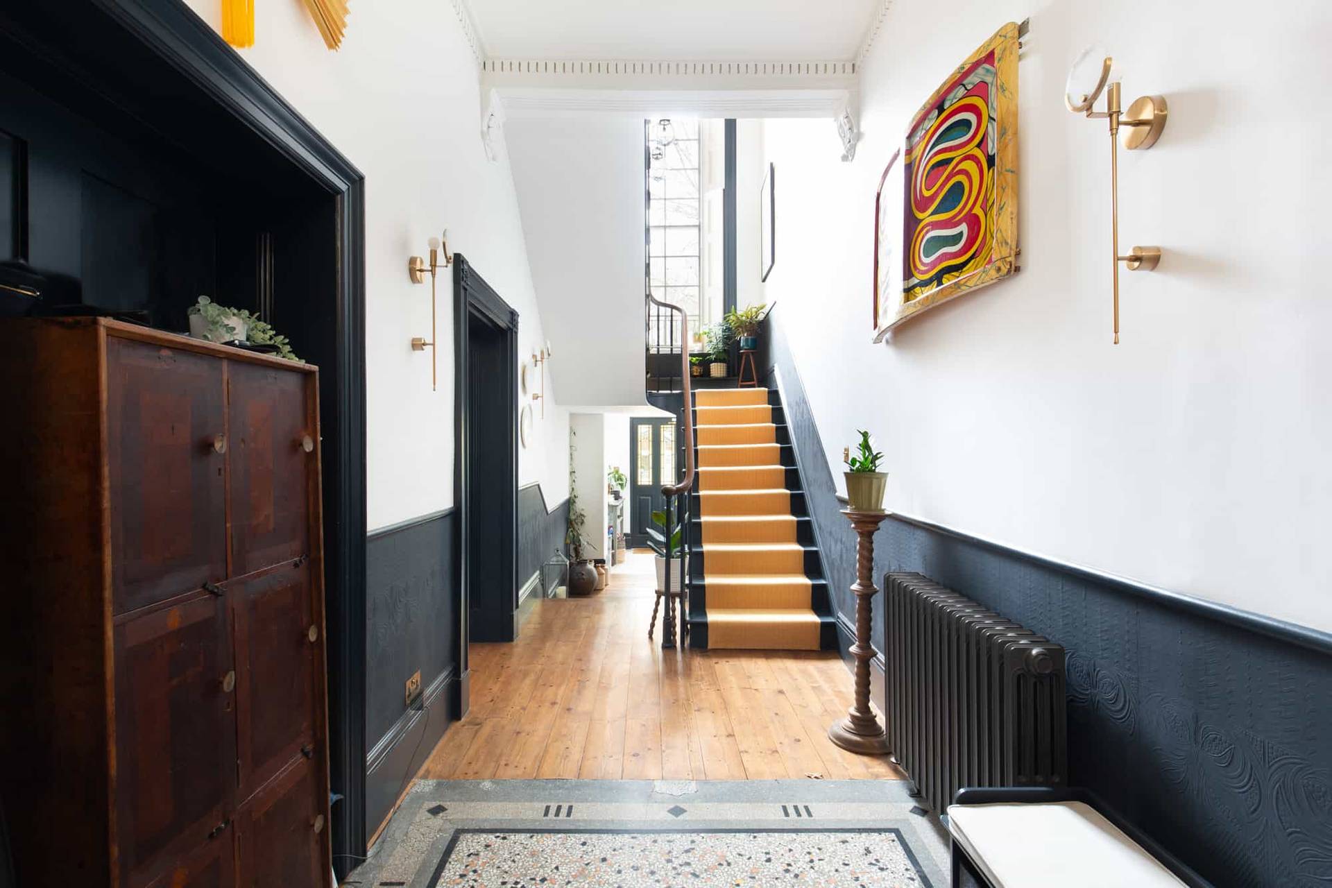 Grand Georgian entrance hall in Camberwell, SE5 with half-painted black walls, wooden floors, and staircase via Love Locations.