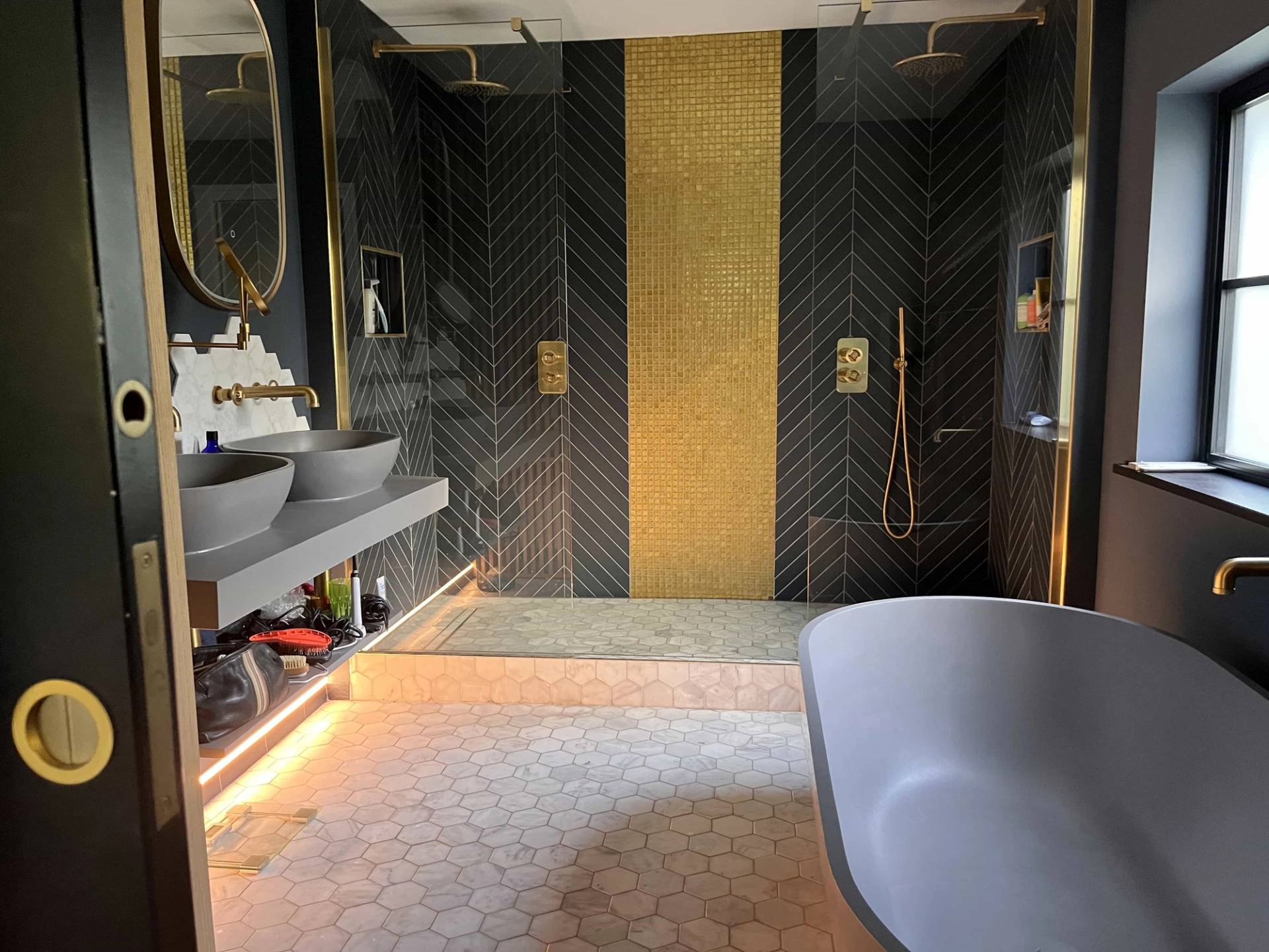 Luxury spa bathroom featuring double vessel sinks, gold shower fittings, under-cabinet lighting, and a dark stone bath, Love Locations GU3.