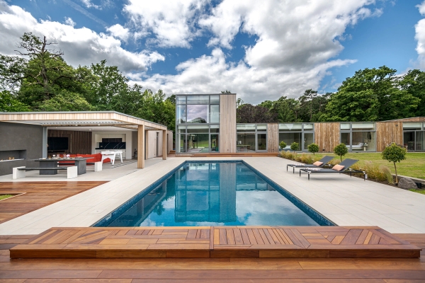 Love Locations resort style location Surrey: Direct eye-level perspective down a crystal blue lap pool featuring sun loungers and an open pavilion pool house, perfect for holiday-themed commercials.