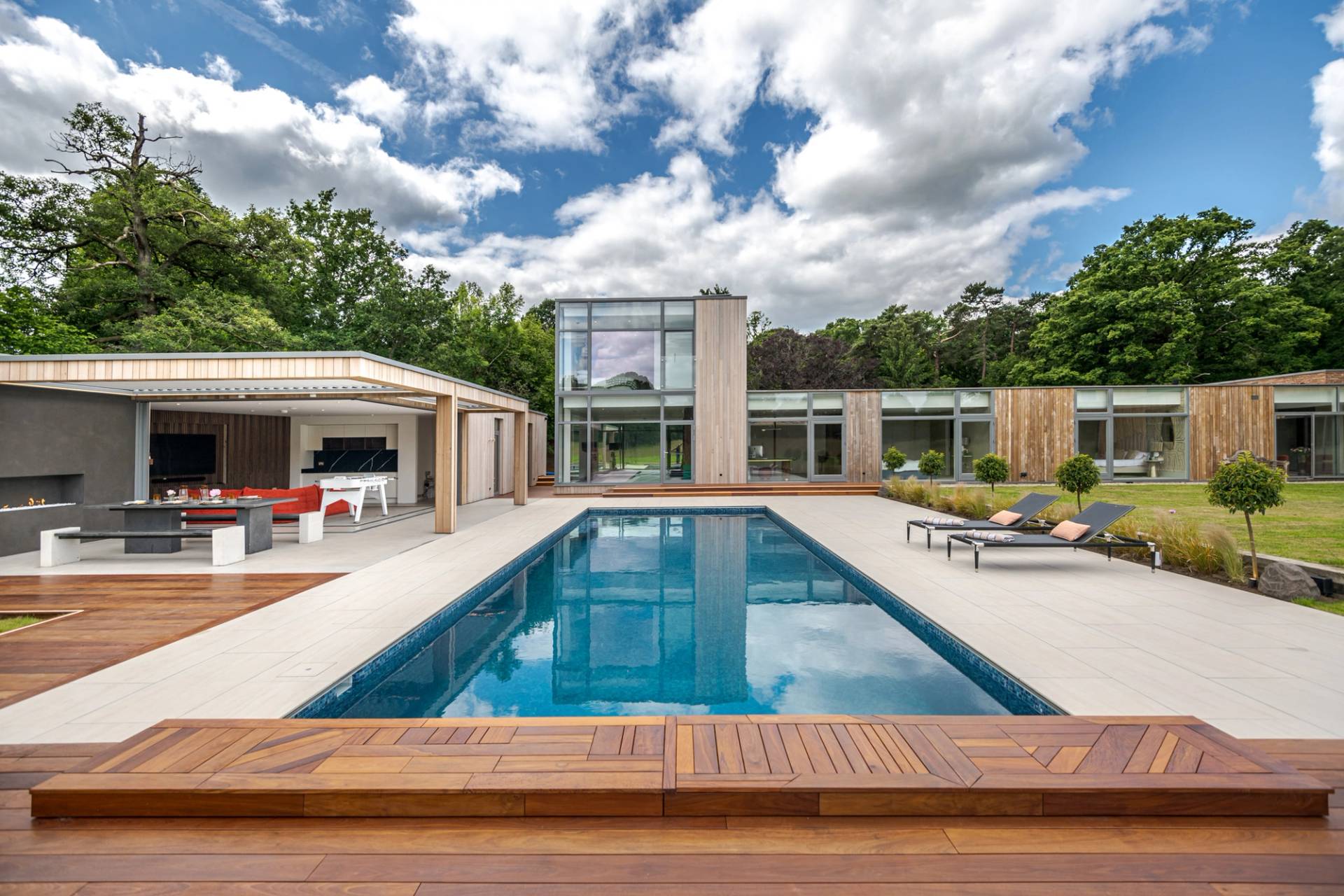 Love Locations resort style location Surrey: Direct eye-level perspective down a crystal blue lap pool featuring sun loungers and an open pavilion pool house, perfect for holiday-themed commercials.