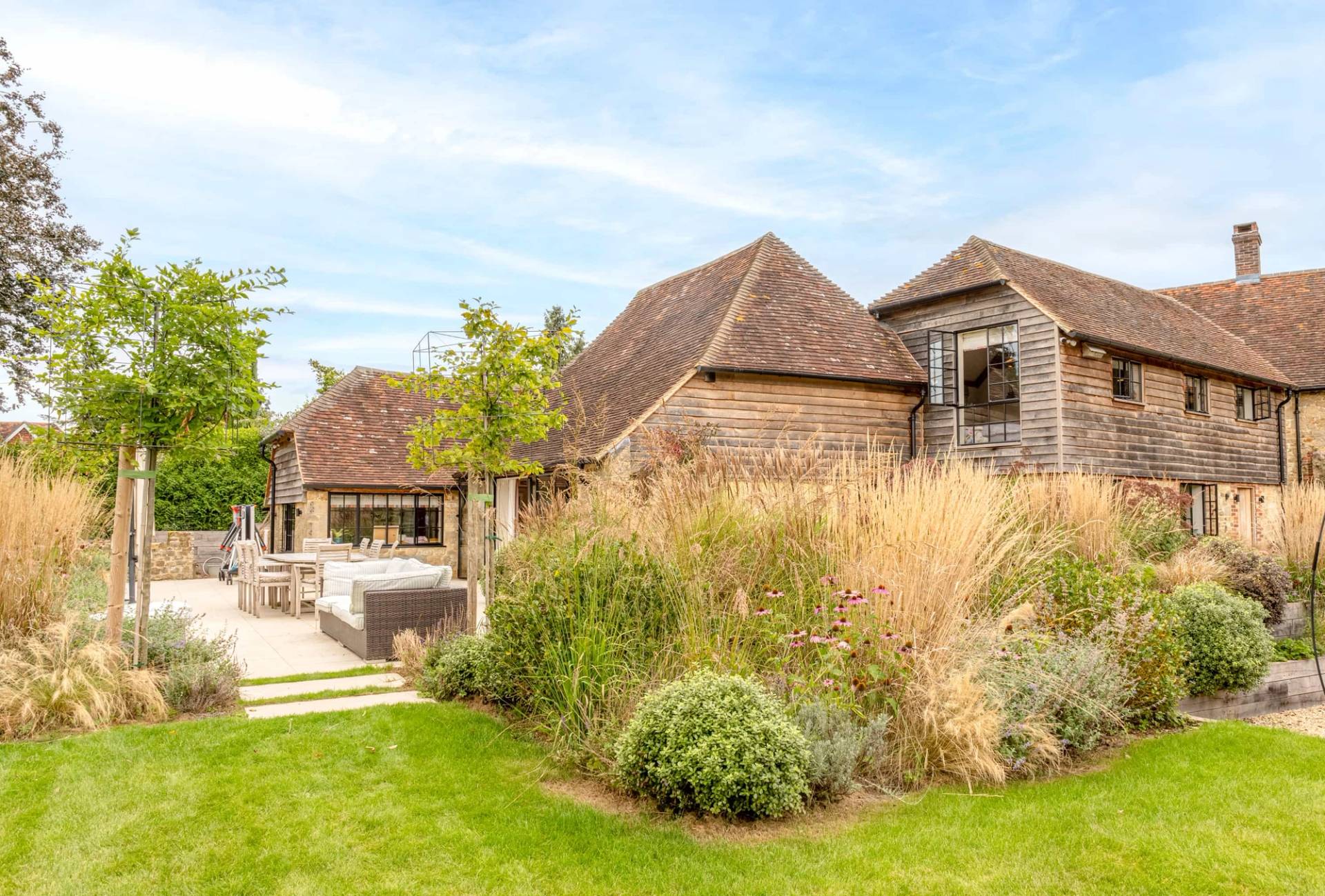 Converted Sussex barn exterior showing weatherboard cladding and prairie garden landscaping, Love Locations GU28.