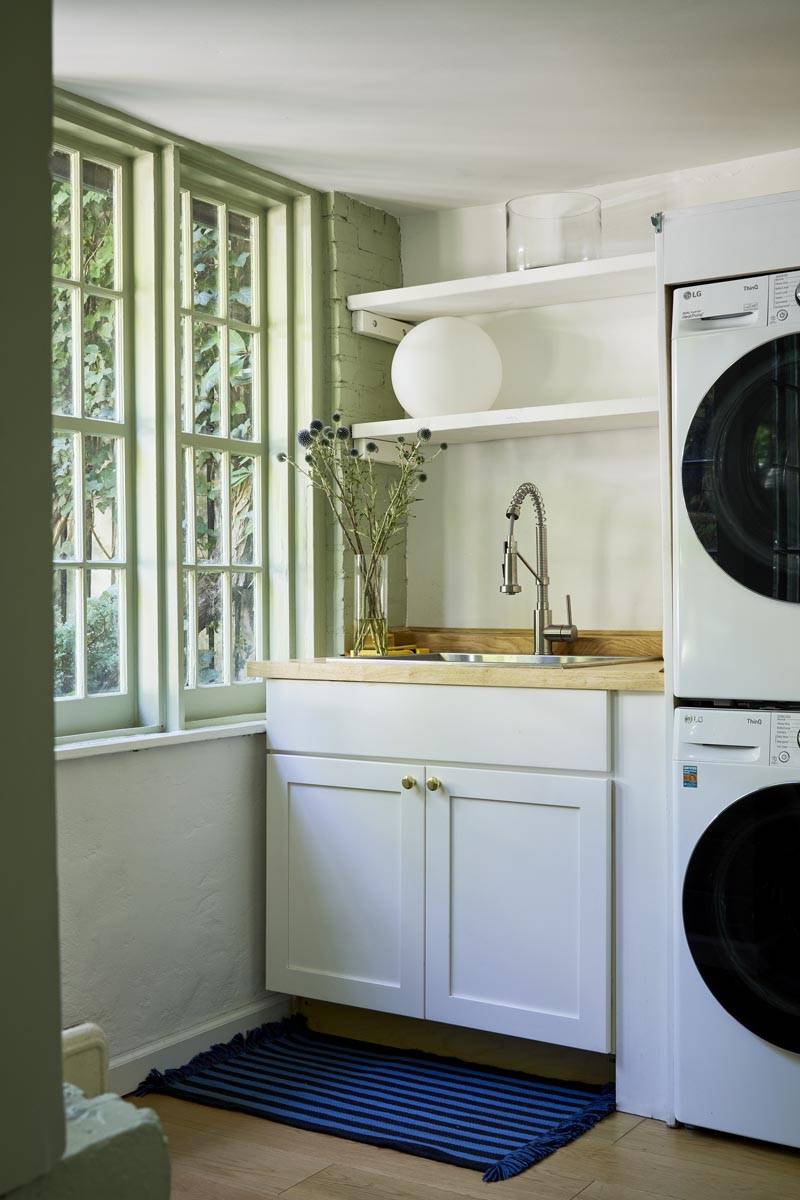 Light-filled kitchen and laundry nook photoshoot venue in Manhattan New York available via Love Locations, featuring white cabinetry, stacked washer-dryer, and a sunlit sash window.