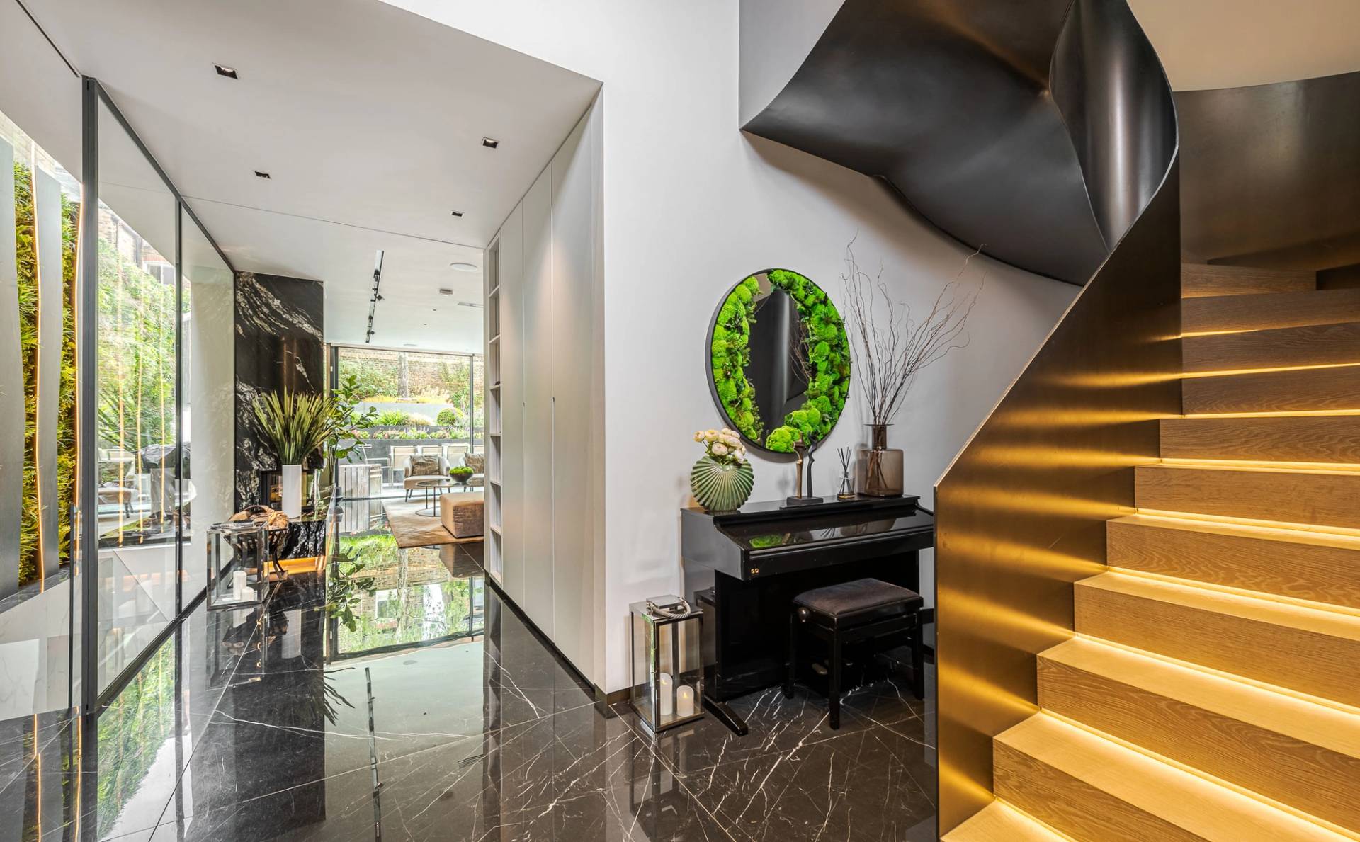 Hallway entrance with a upright black piano, green moss wall art, and a dark helical metal staircase, Love Locations SW11.